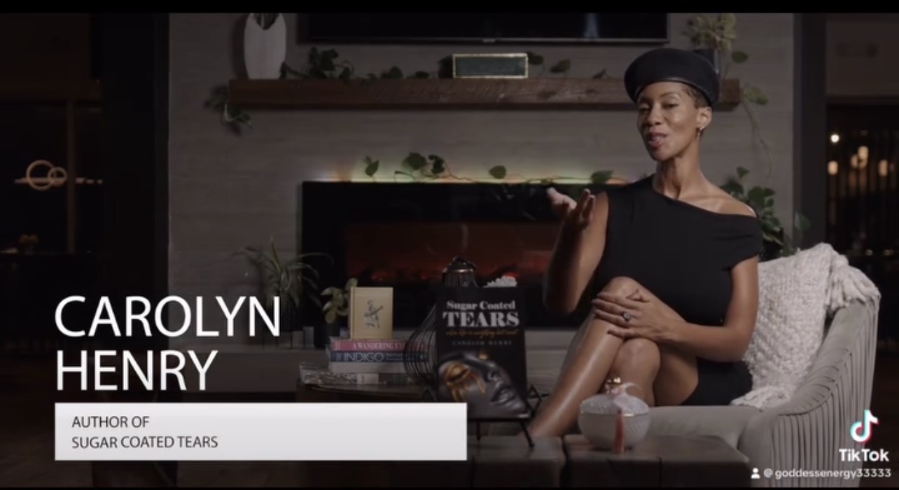 Woman sitting on a couch in a room with books and plants, speaking during an interview, with text overlay about Carolyn Henry.