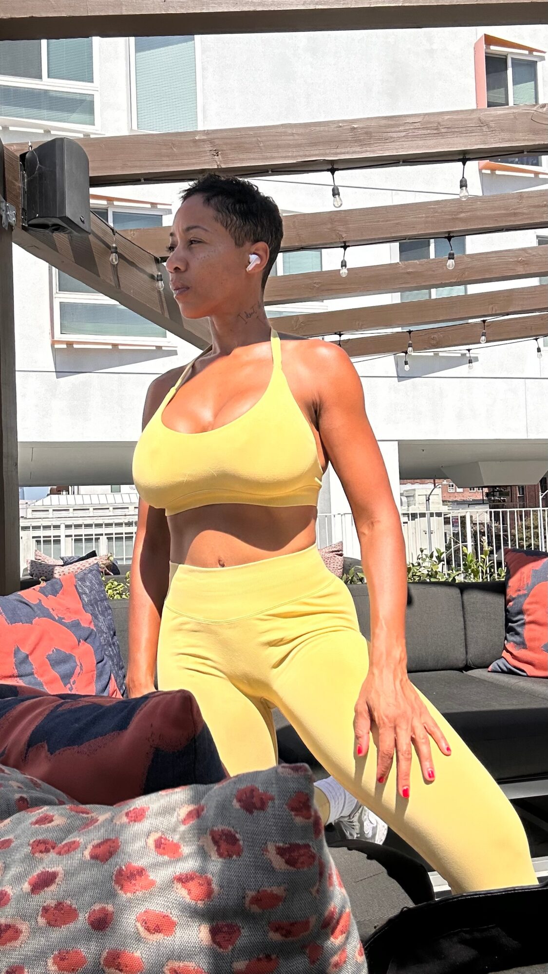 Woman in yellow crop top and pants standing outdoors with modern buildings in background.