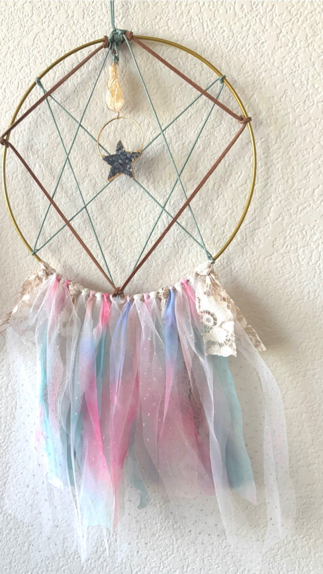 Dreamcatcher with a star, hanging feathers, and pastel-colored ribbons against a wall.
