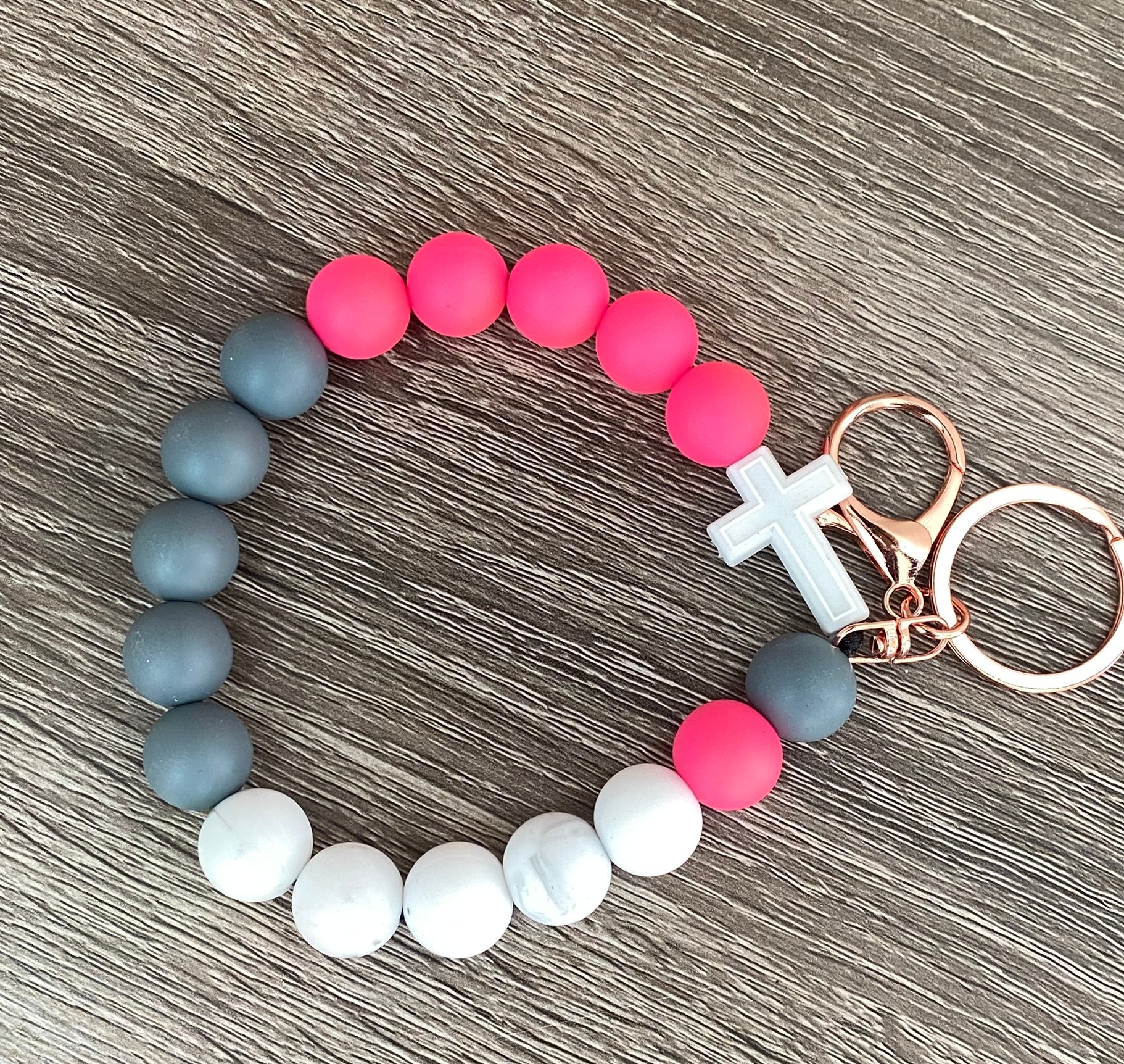 Beaded bracelet with pink, gray, and white beads, and a white cross charm, on a wooden surface.