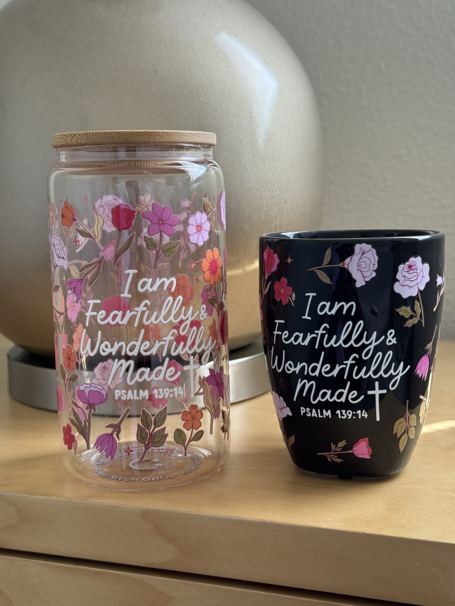 Glass jar and black mug with floral designs and inspirational text on a wooden surface.