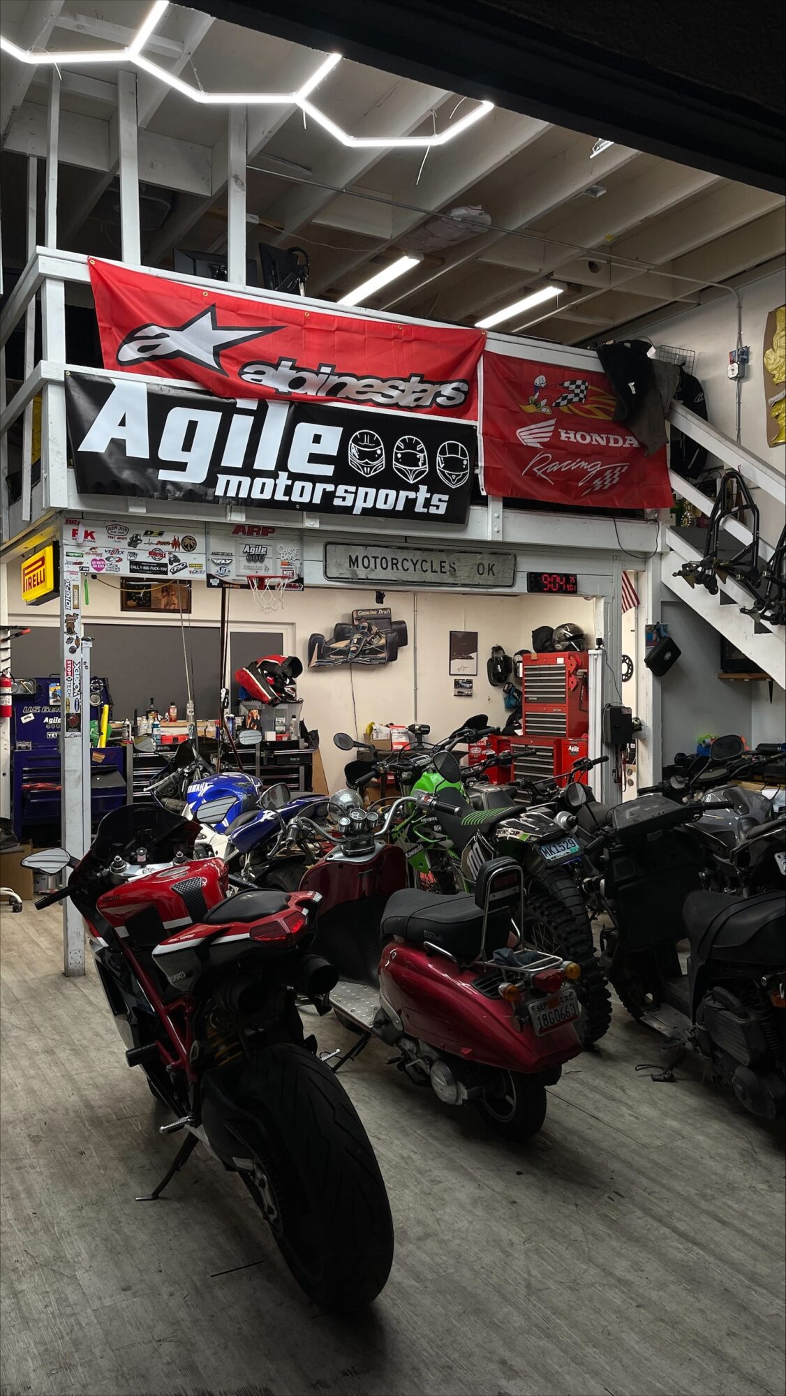 Indoor motorcycle showroom with bikes, banners, and a staircase, featuring a large red and black banner for Agile Motorsports.