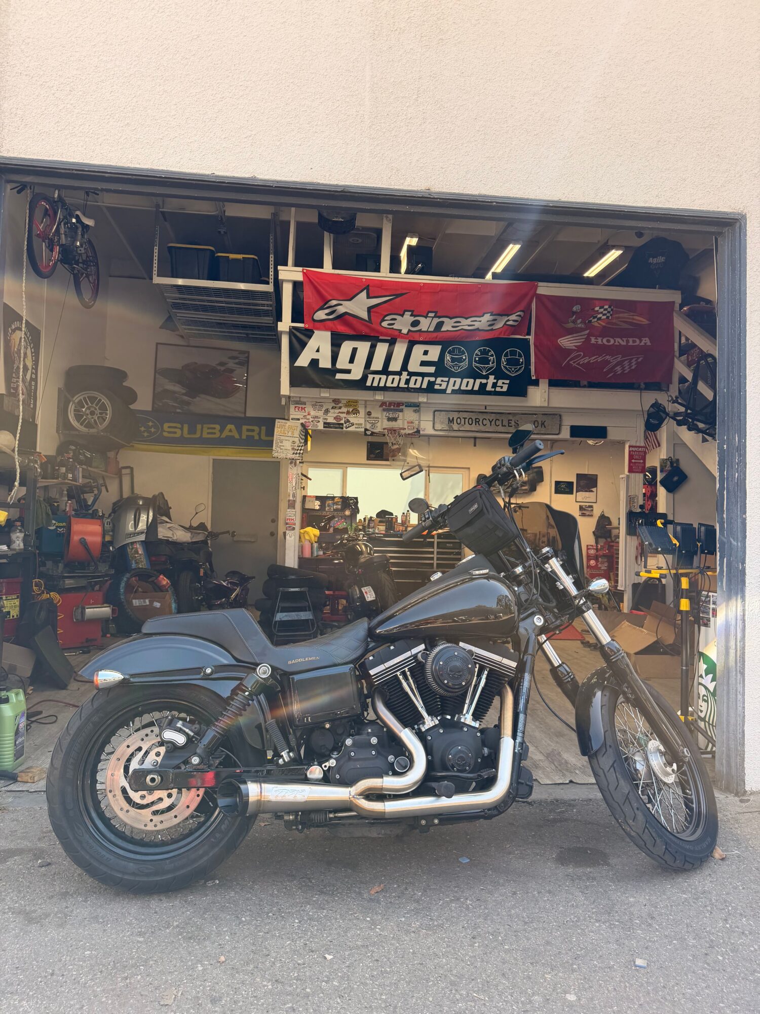 Motorcycle parked outside a garage with tools and equipment inside, viewed from the side.