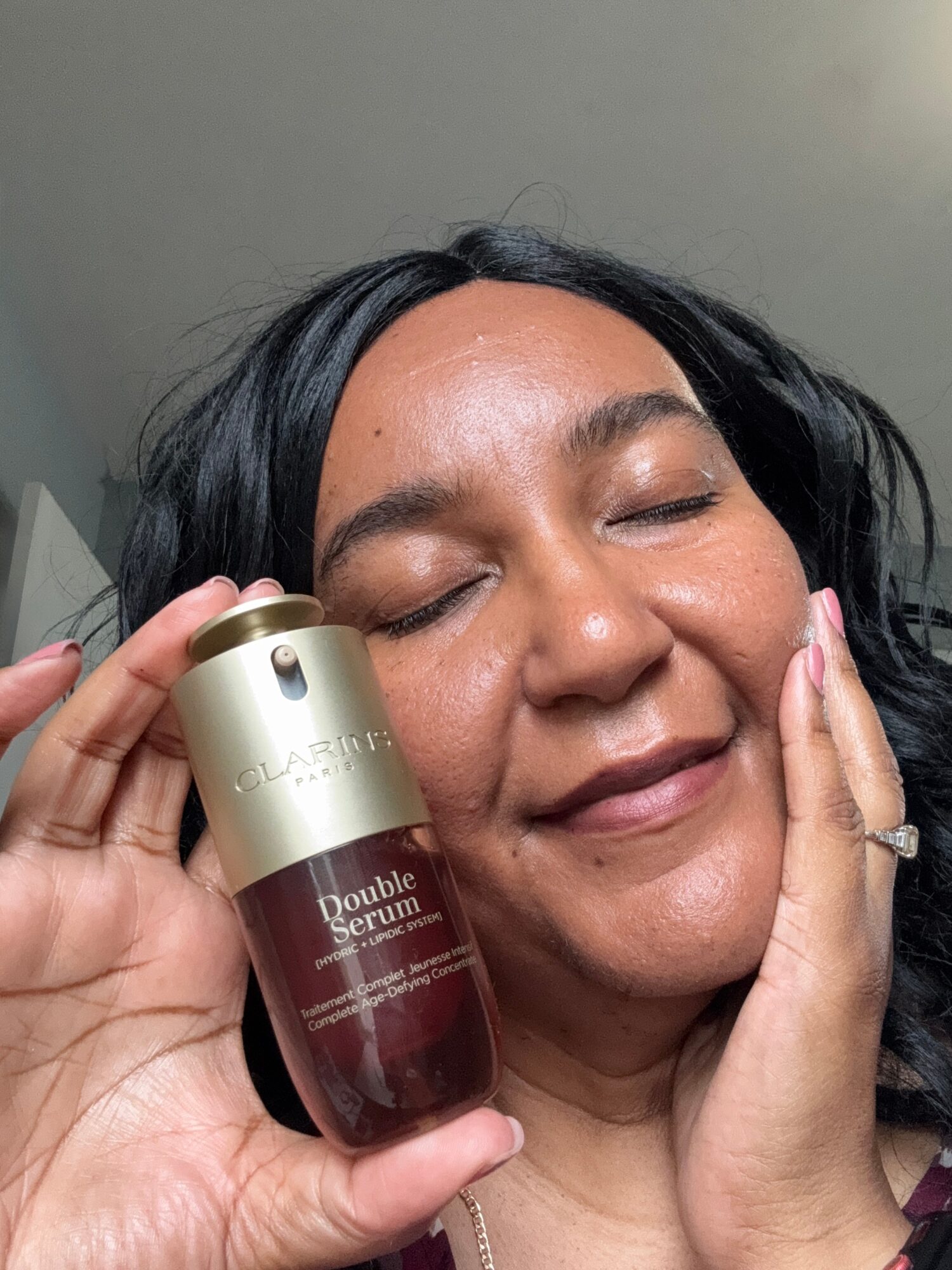 Woman with closed eyes holding a skincare product close to her face, smiling gently, indoors.
