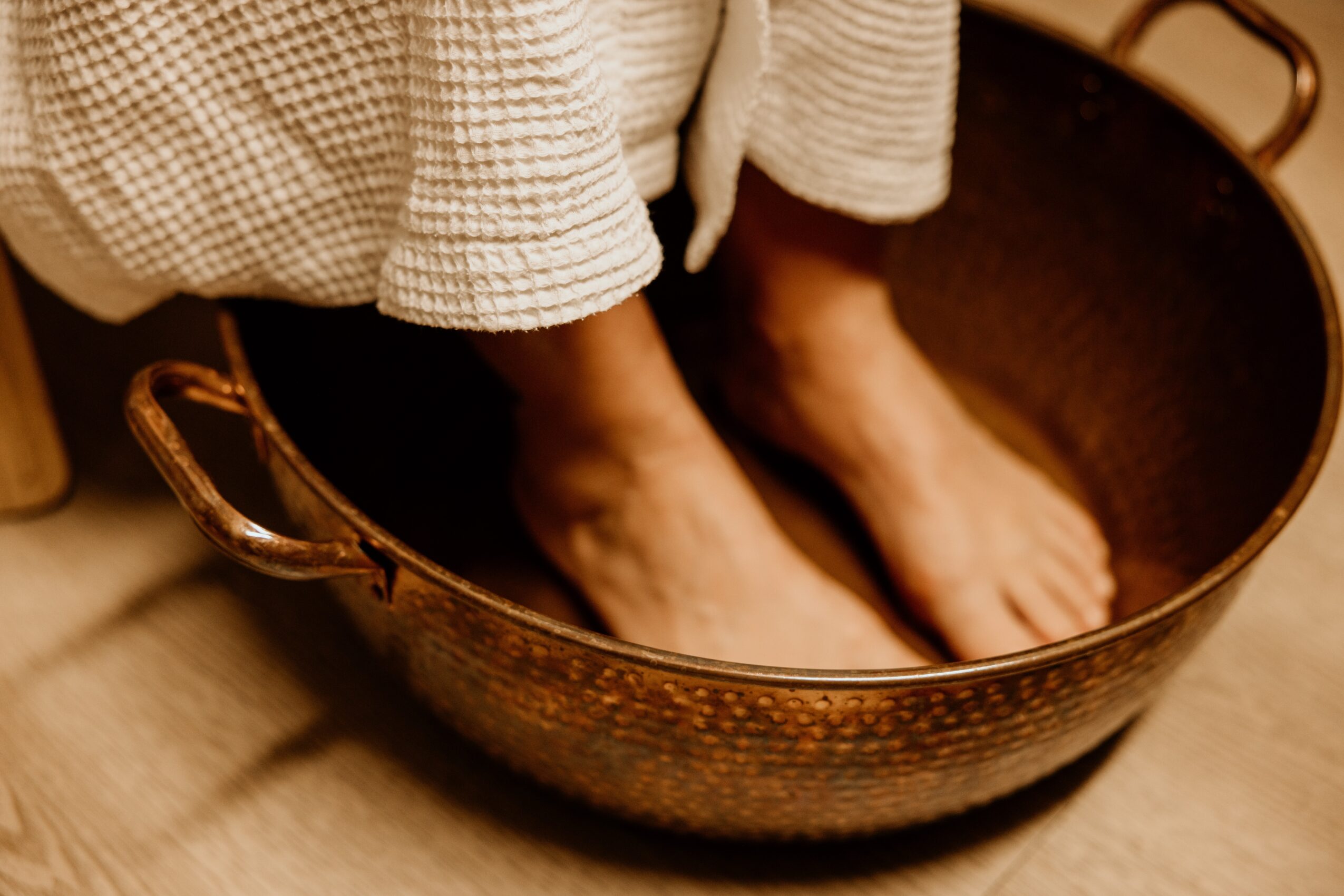 Person soaking feet in a copper basin, wearing a checkered garment, with feet submerged in water.