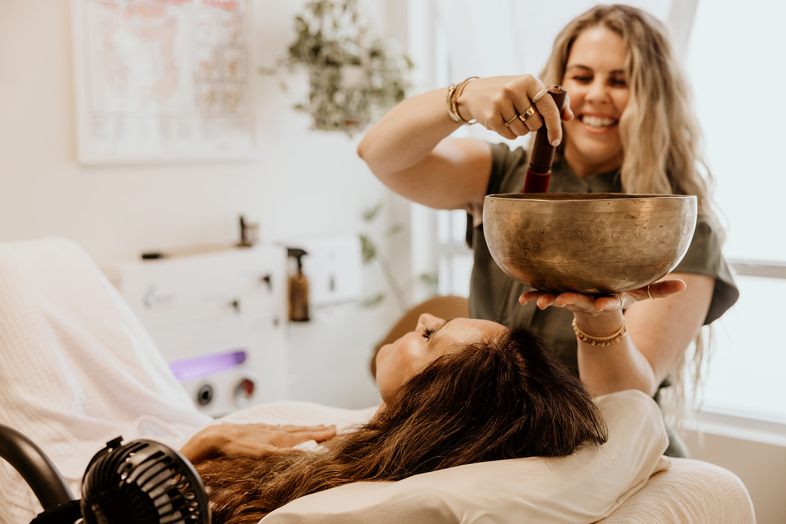 Woman smiling and holding a large bowl, woman lying on a bed with head resting on pillow, in a bright room.