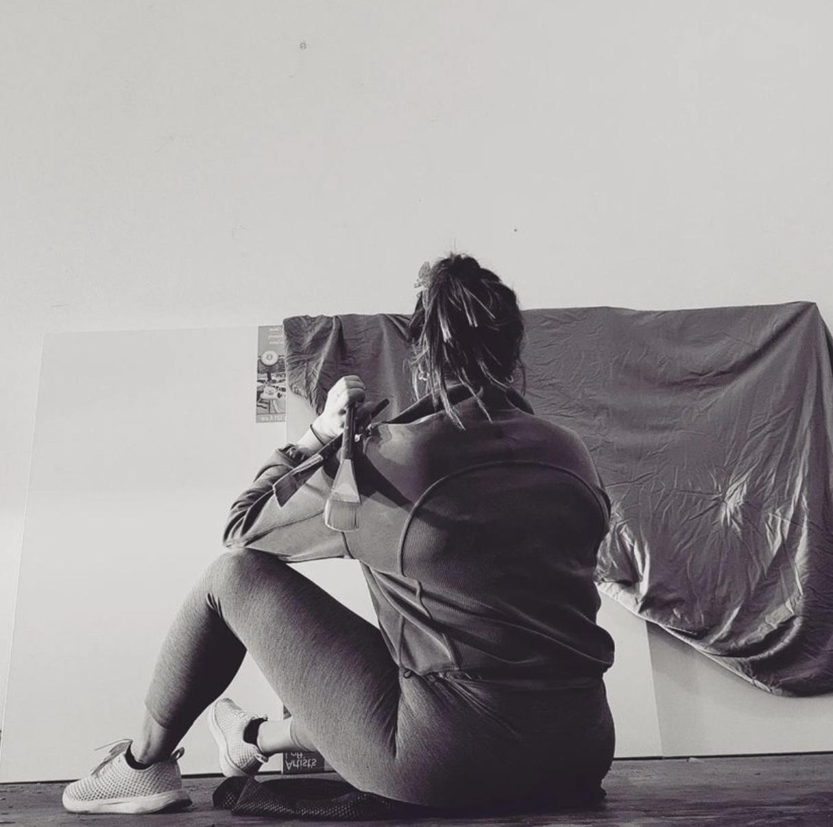 Person sitting on the floor, facing away, with a cloth draped on the wall behind them.