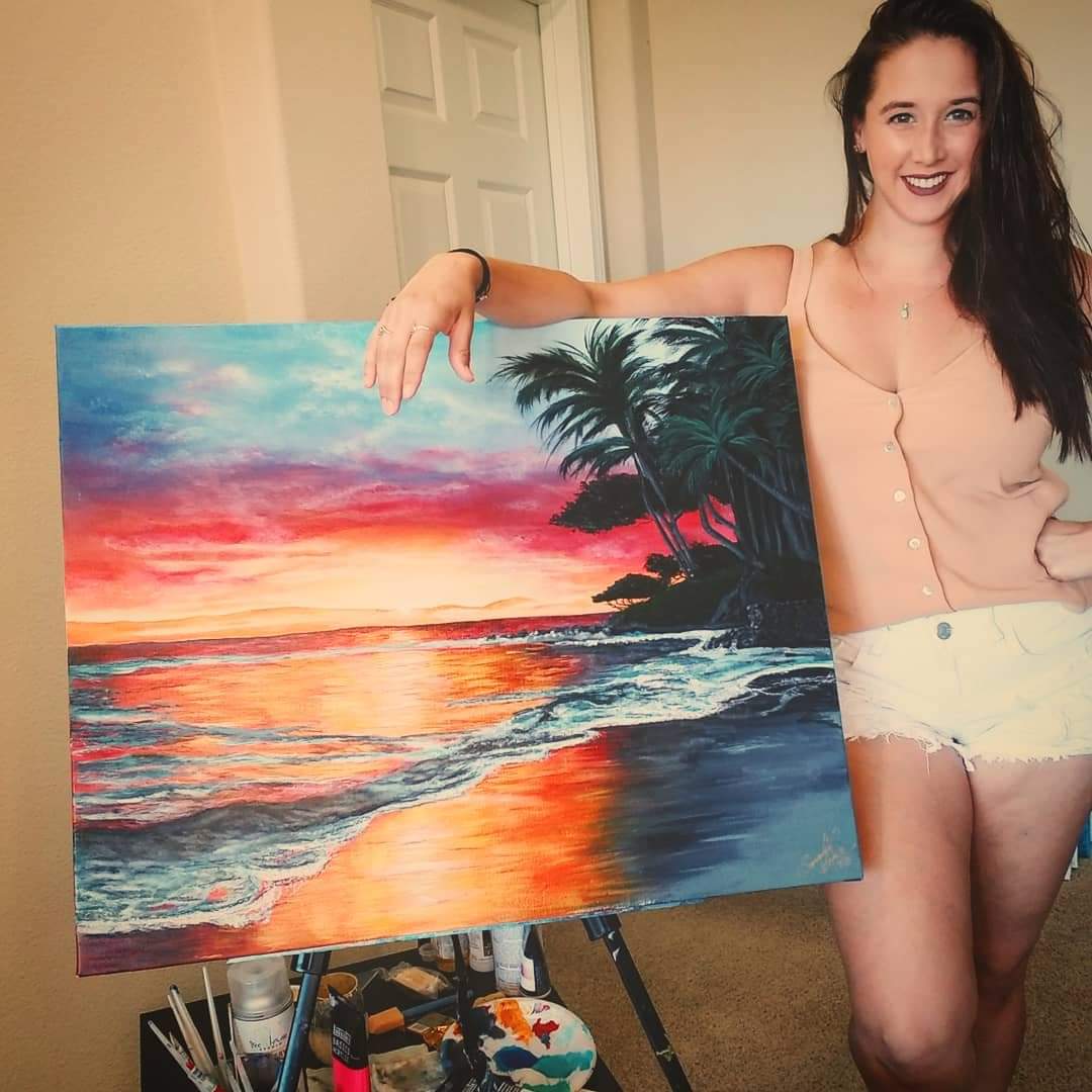 Young woman with long dark hair smiling, holding a colorful sunset beach painting indoors.