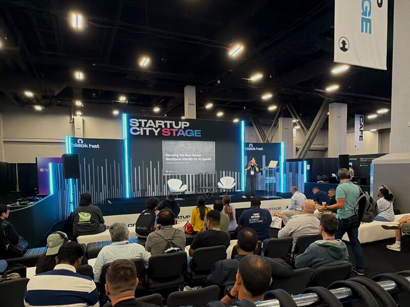 Conference stage with a speaker presenting to an audience in a large indoor event space.