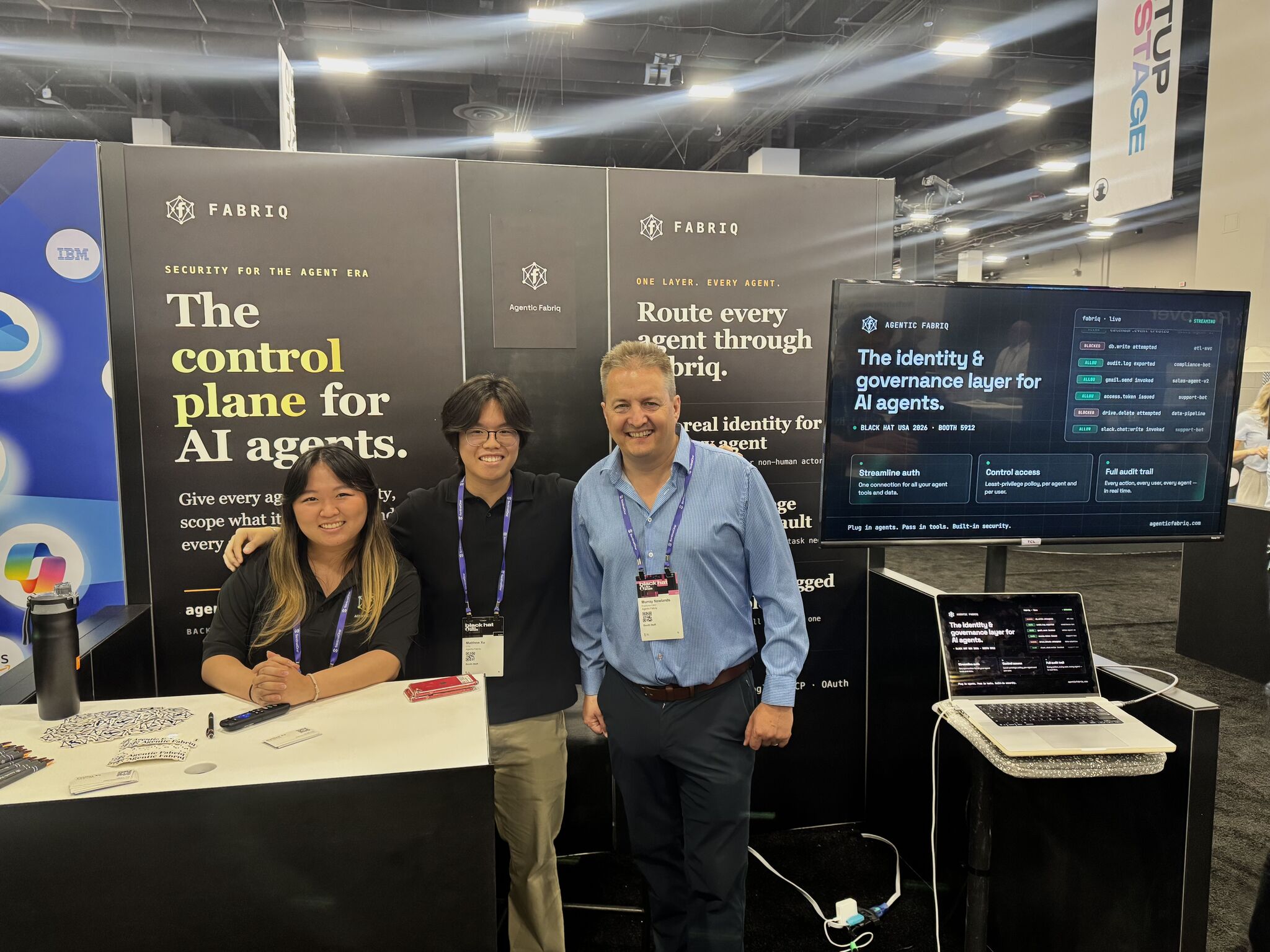 Three people standing in front of a booth with banners about AI agents and control plane, smiling at the camera.