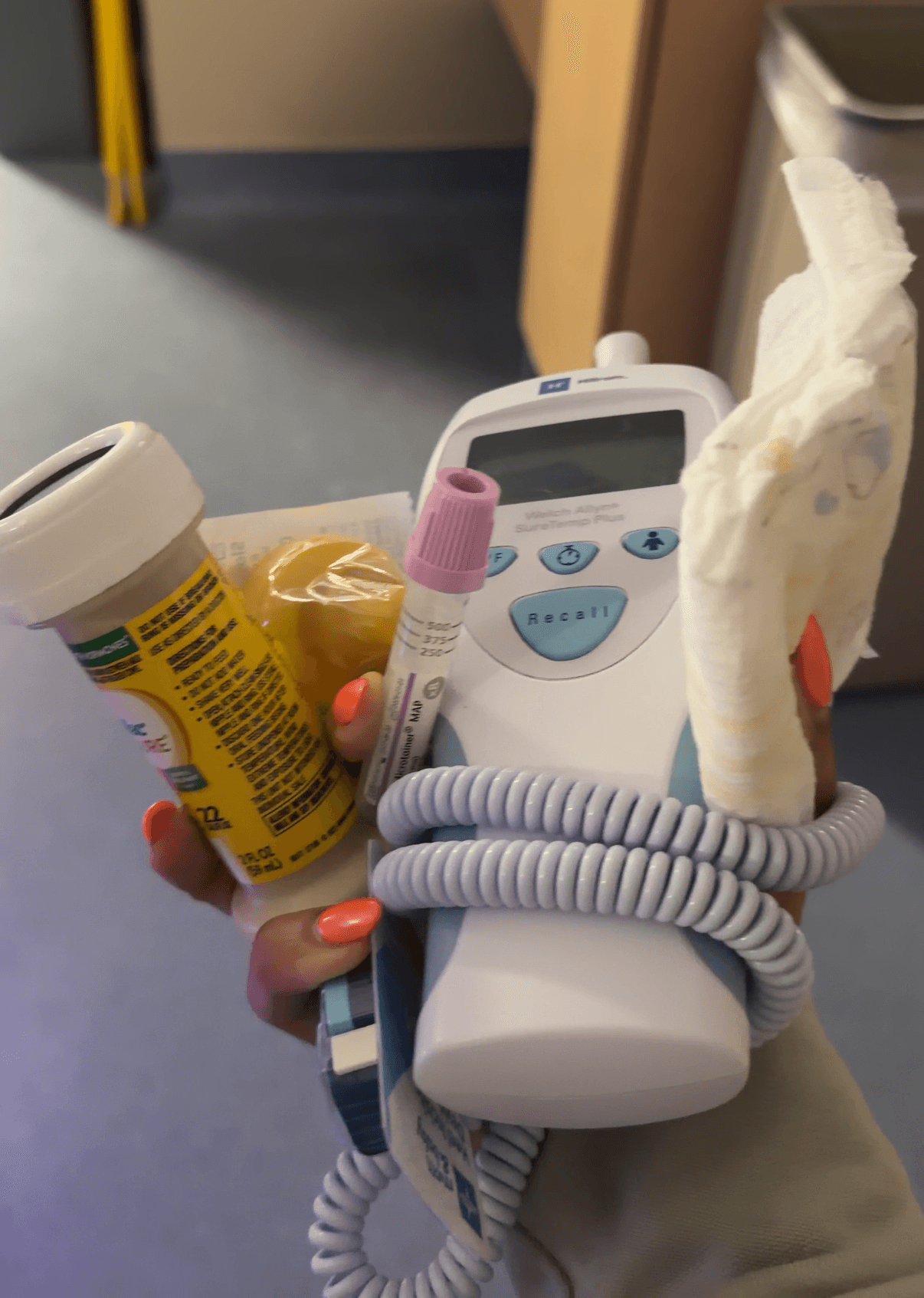 Hand holding a medical device with a coiled cord, medication bottle, and tissue, in a clinical setting.