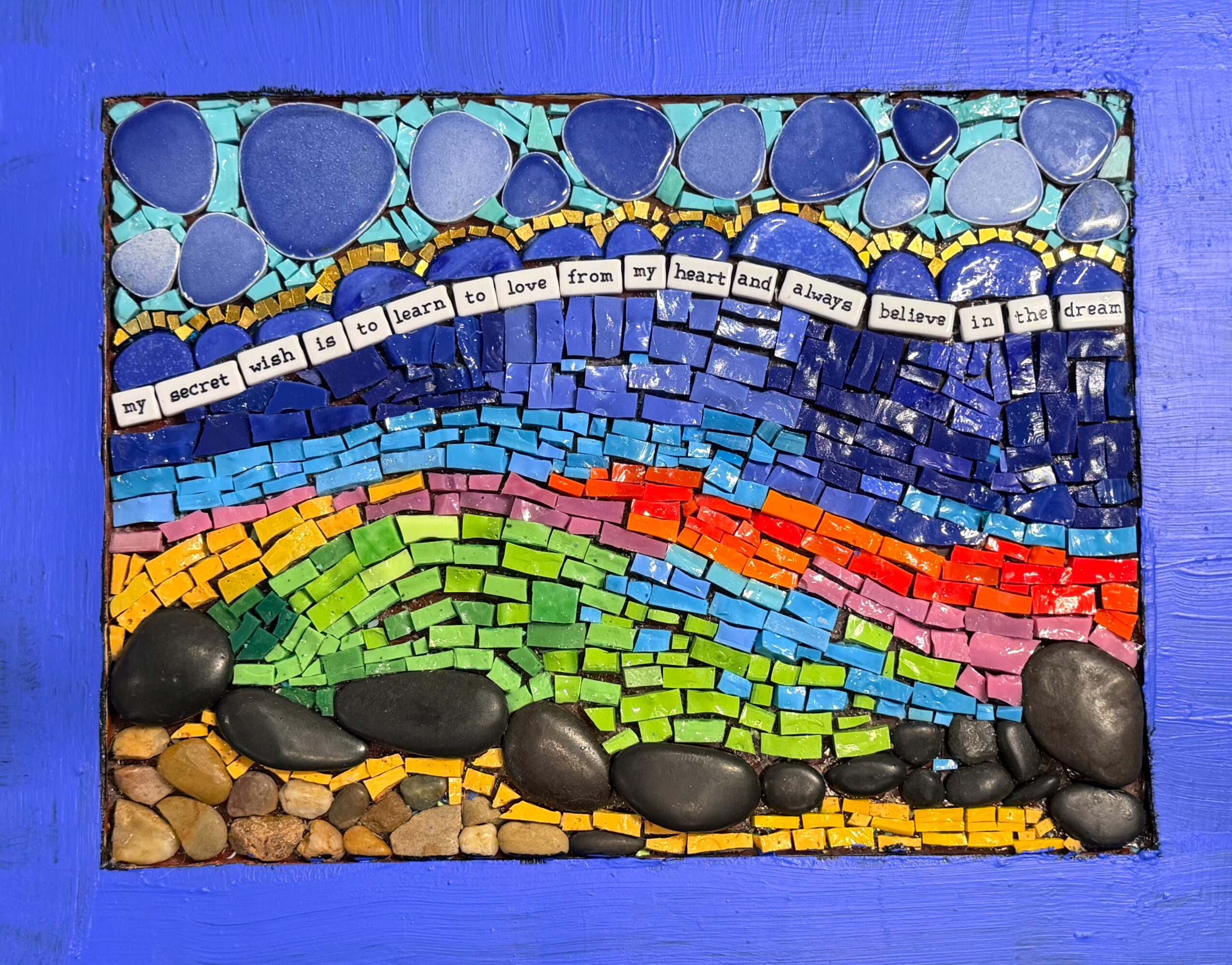 Colorful mosaic with a rainbow, stones, and a quote about love and hope, framed in blue, with a textured background.
