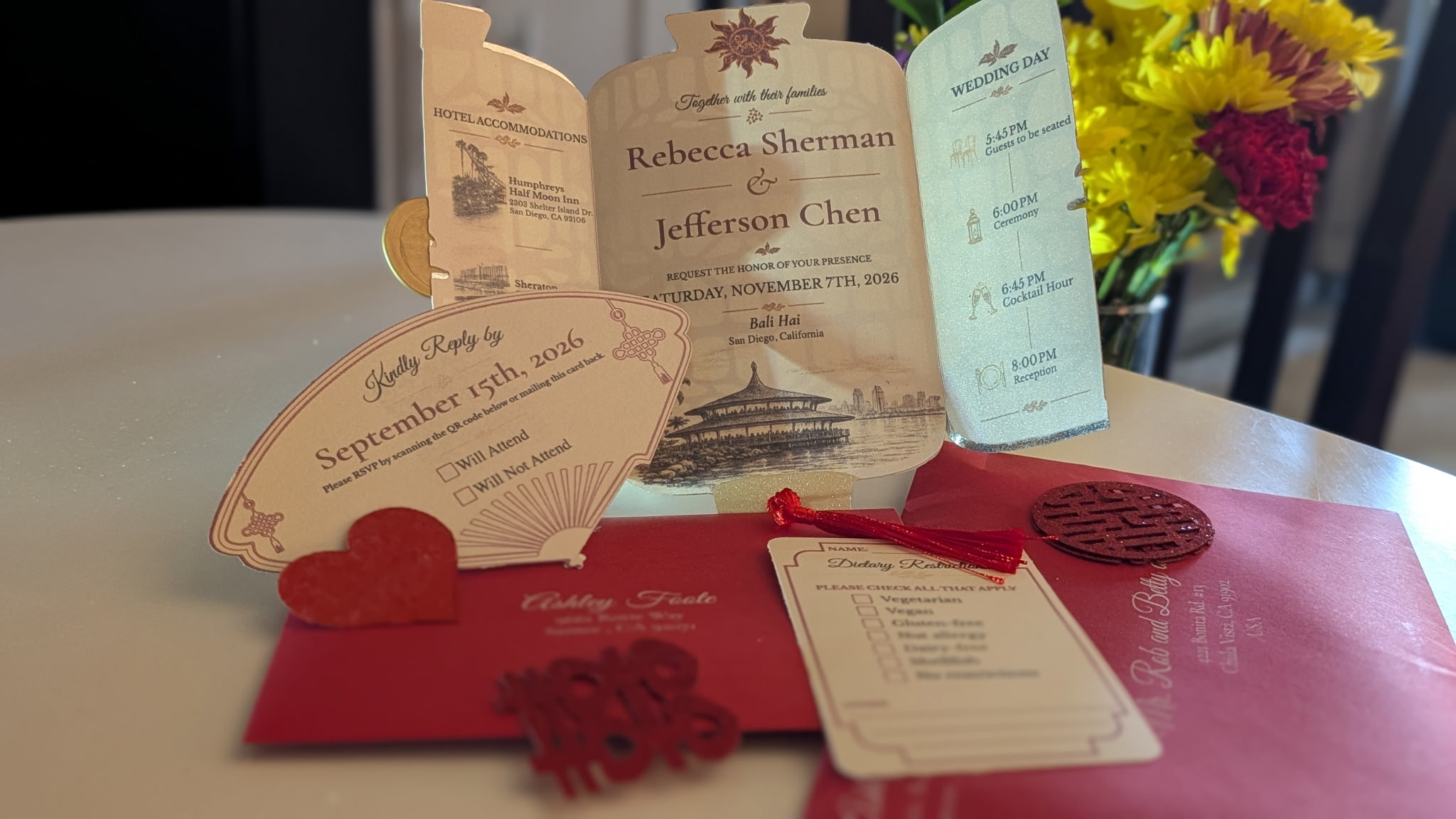 Wedding invitation, red envelope, and flowers on a table, with a blurred background.
