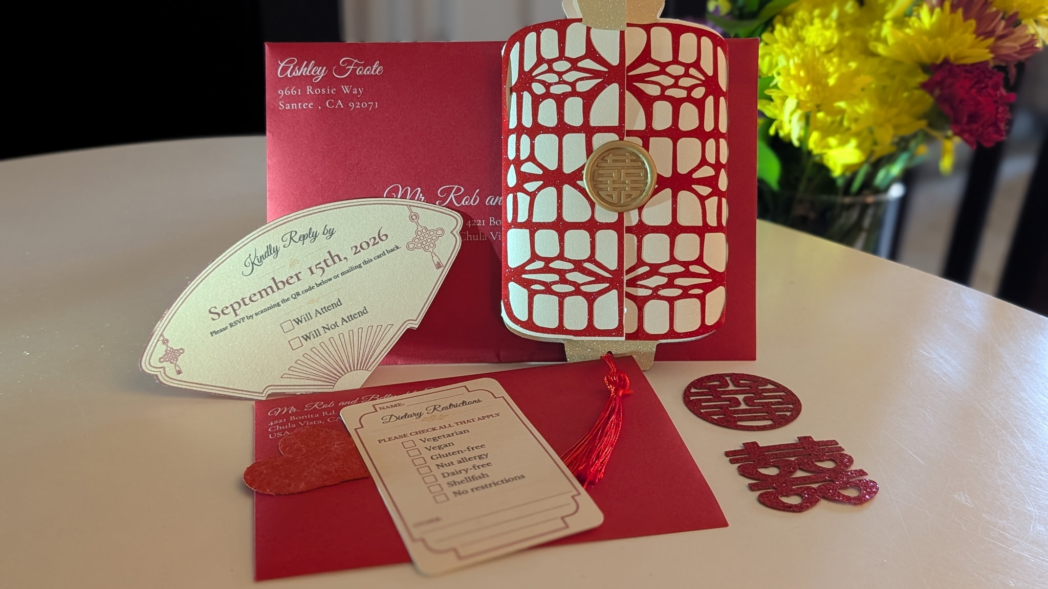 Open red and white card with decorative cutouts, surrounded by event tickets, a red envelope, and small decorative items on a table.
