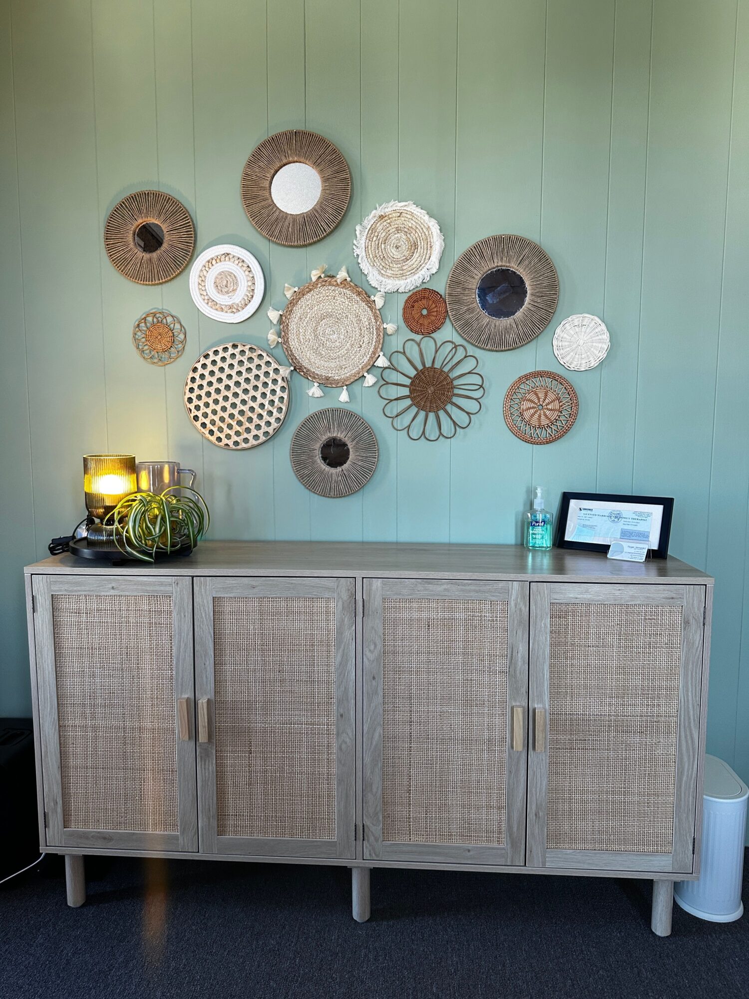 Wall decorated with circular woven art pieces, a cabinet with rattan doors, and a small table with a lamp and plant.