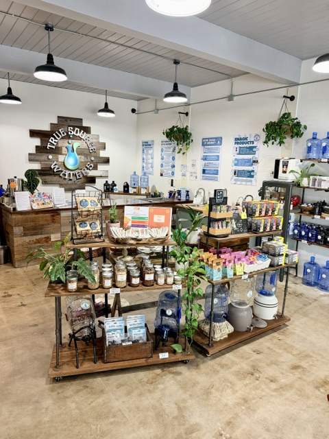 Interior of a store with shelves and displays of products, a sign with a blue water drop, and hanging plants.