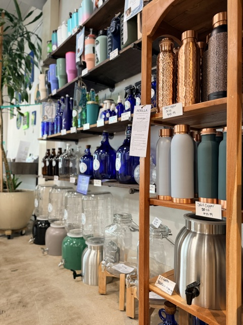 Shelves filled with colorful bottles and containers, with a wooden rack holding thermoses and water bottles, in a store.