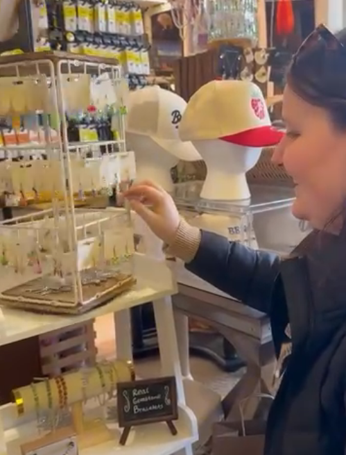 Woman shopping for jewelry or accessories in a store, with hats and shelves in the background.