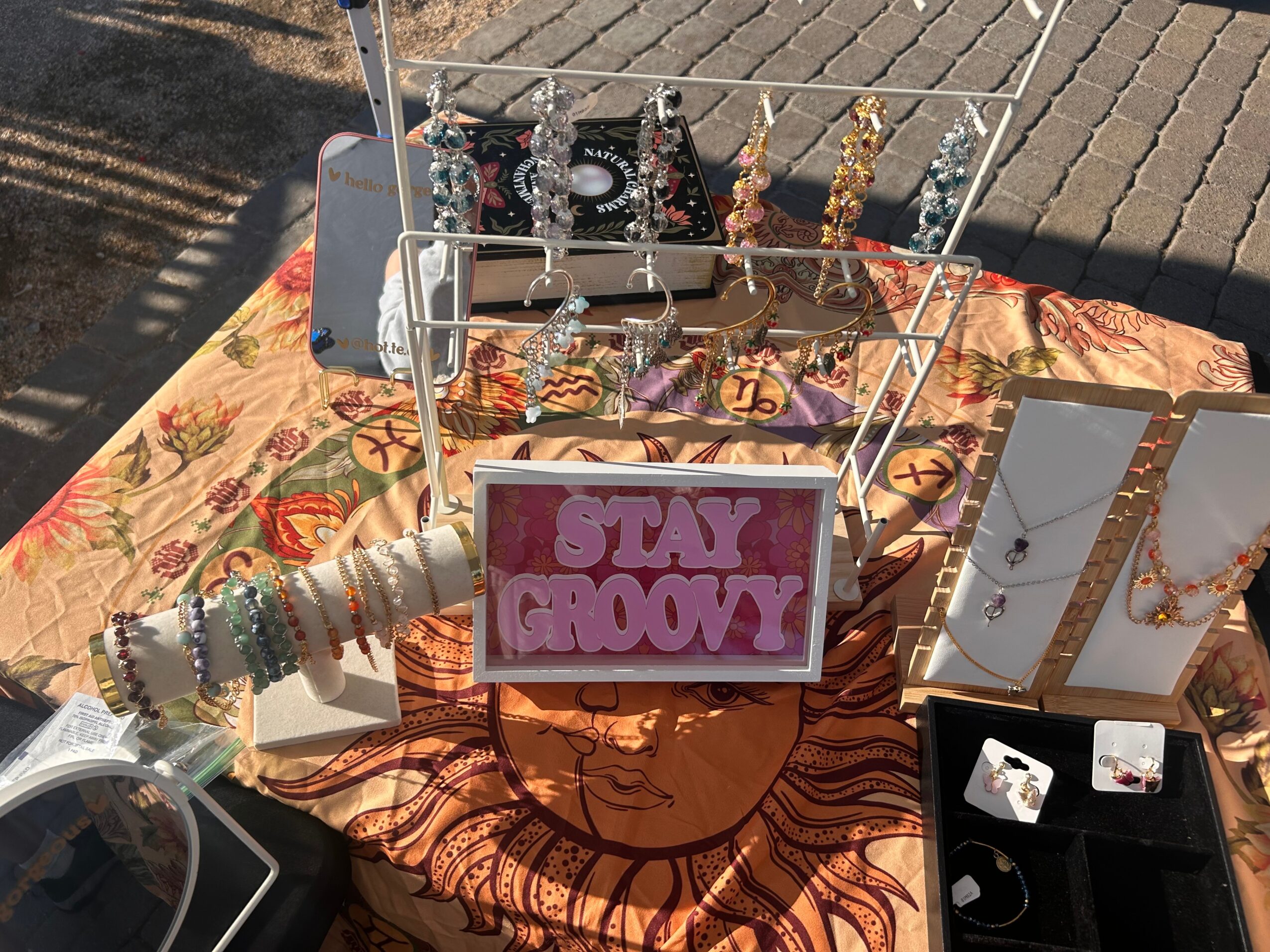 Display of jewelry and accessories on a table with a colorful cloth, including a sign that says 'STAY GROOVY'.