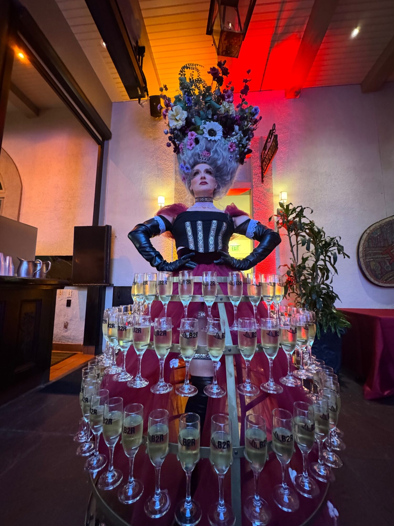 A large sculpture of a woman with an elaborate floral headdress stands behind a table with many champagne glasses, in a decorated indoor setting.