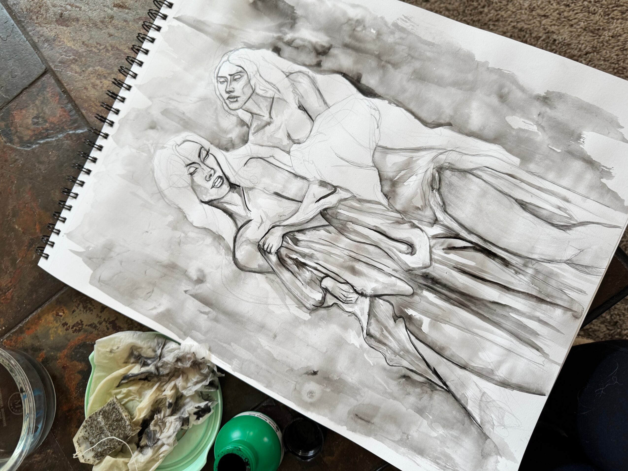 Sketch of two women, one sitting and one standing, with watercolor background, on spiral-bound sketchbook page.
