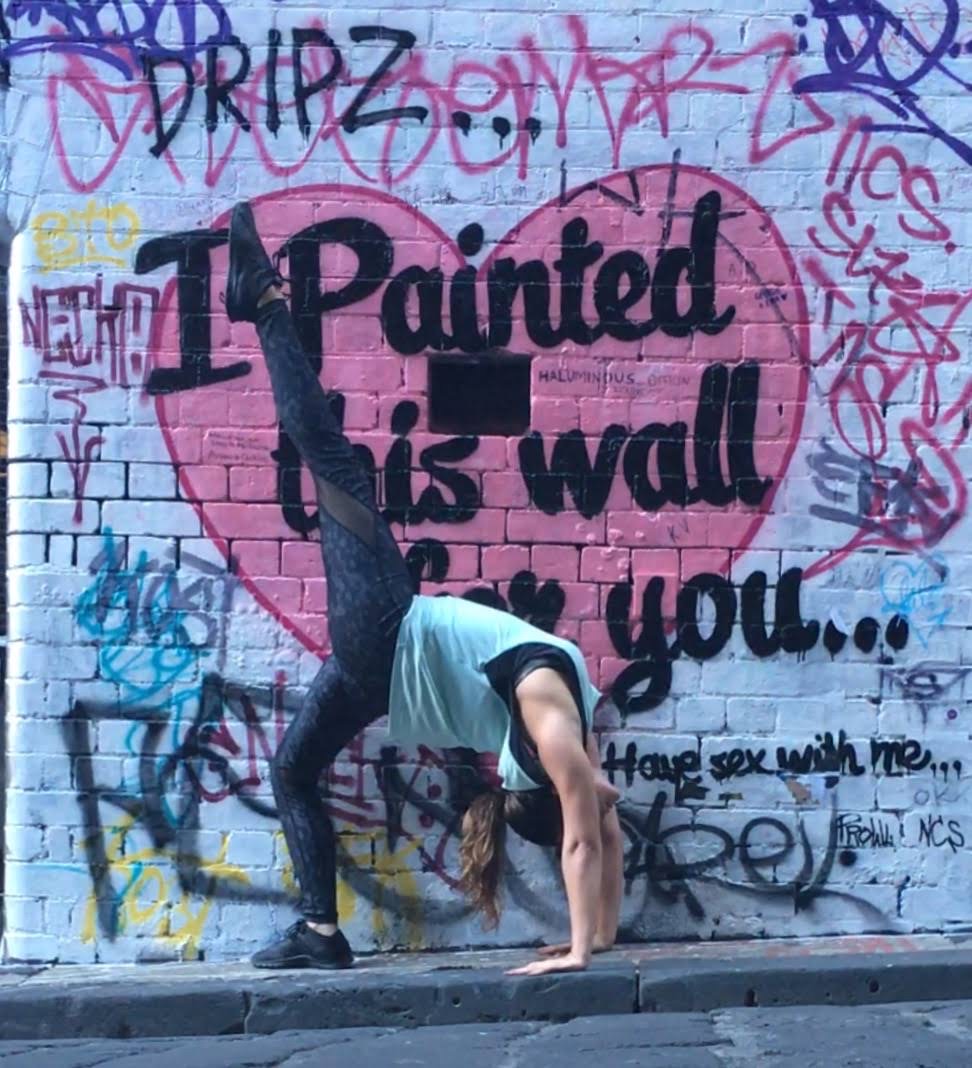 Person doing a handstand against a graffiti-covered wall with a pink heart and text. Word count: 20.