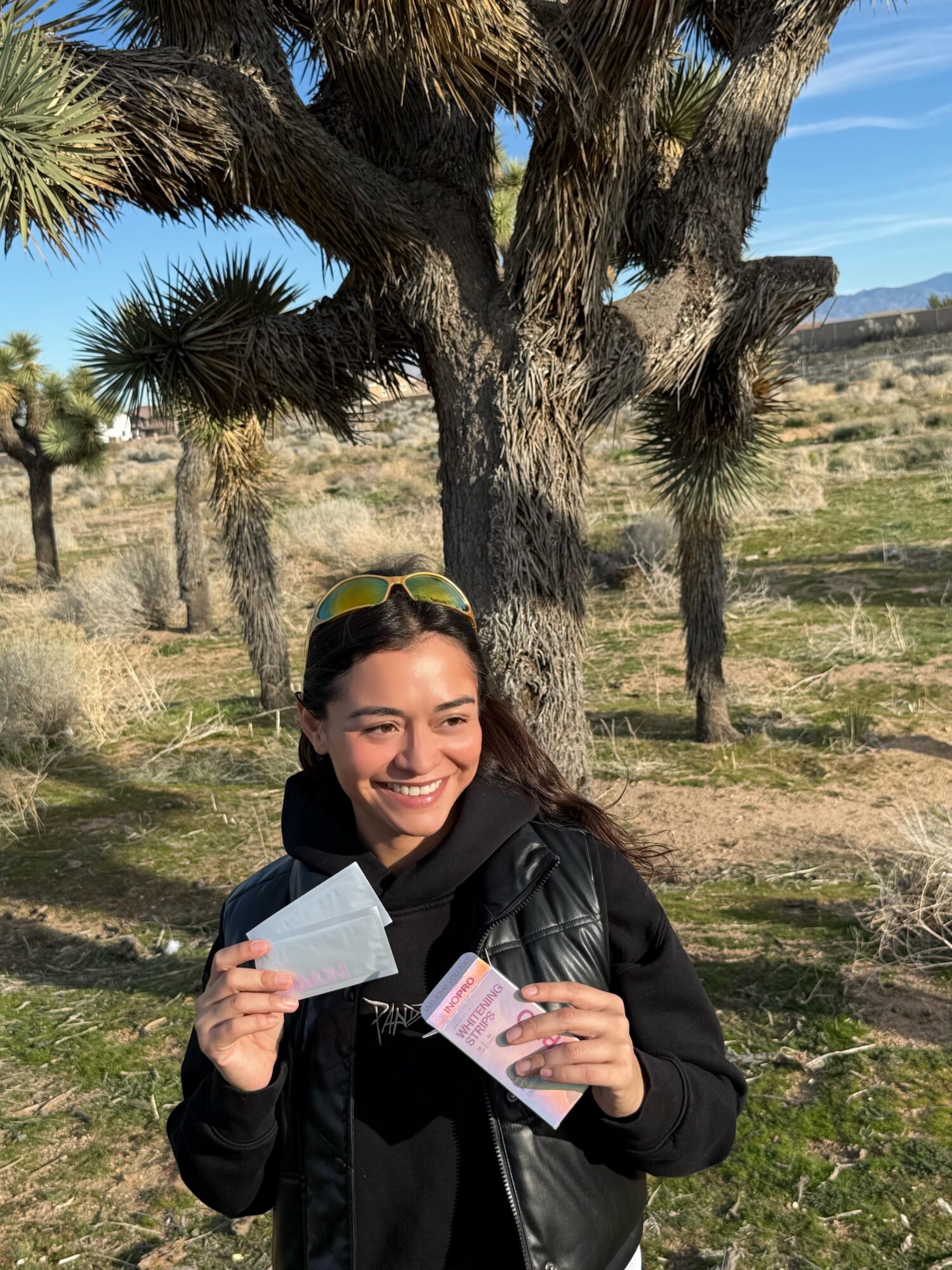 Smiling woman holding tickets outdoors with trees and a landscape in the background.