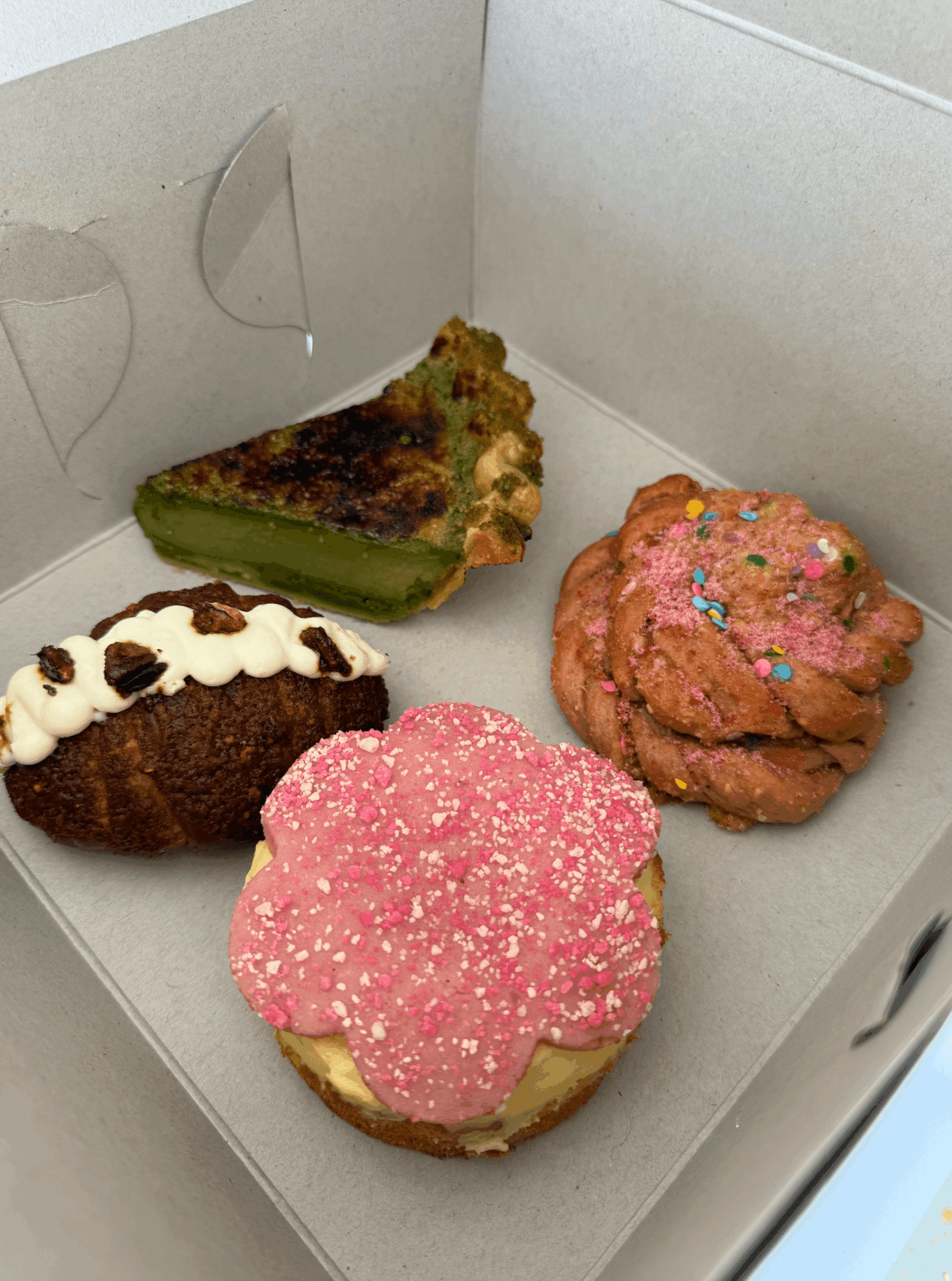 Four decorated cupcakes inside a white box, with various frosting and toppings, on a flat surface.