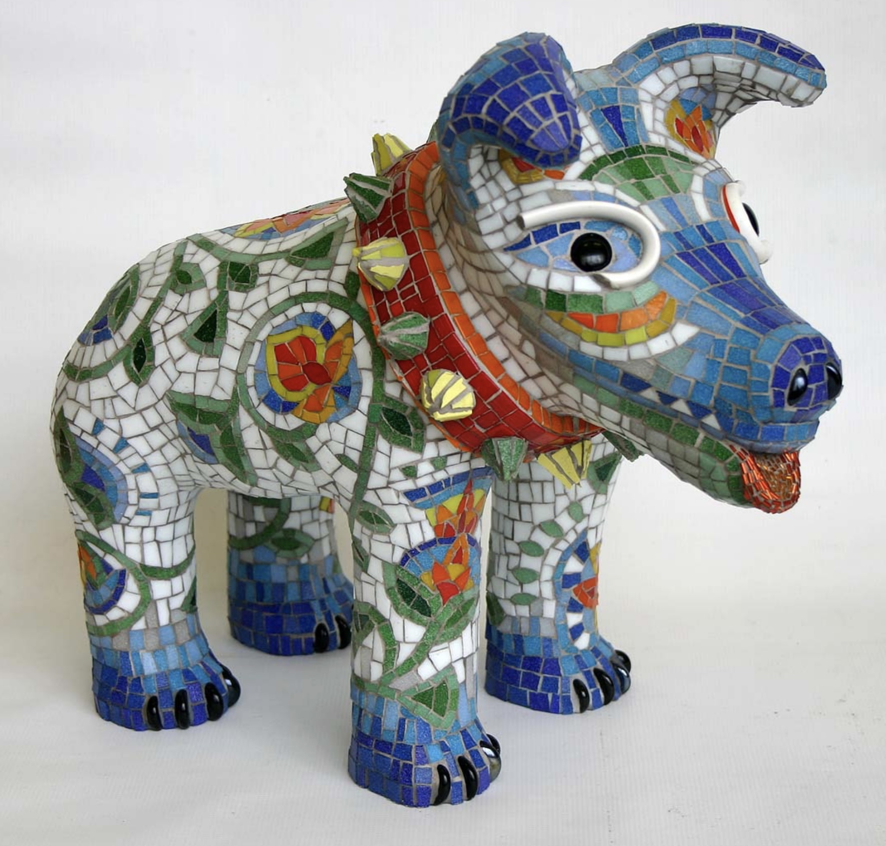 Colorful mosaic sculpture of a dog with a red collar and expressive eyes, decorated with floral and geometric patterns.