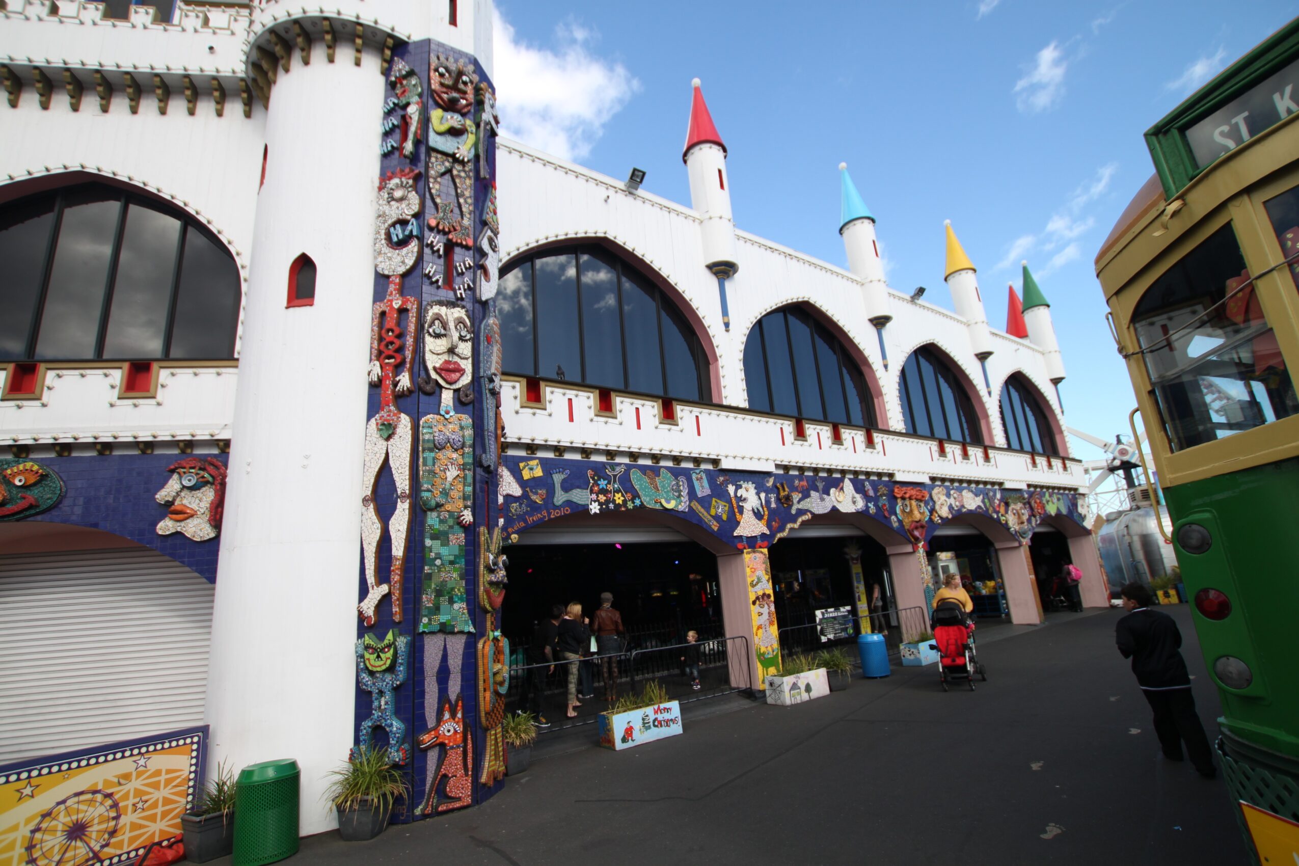 Colorful building with castle-like turrets, large arched windows, and mosaic decorations, with a green trolley on the right side.