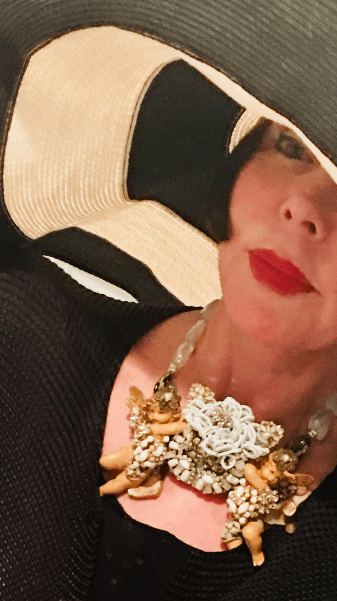 Close-up of a woman wearing a large, ornate necklace and red lipstick, with part of her face and shoulder visible.