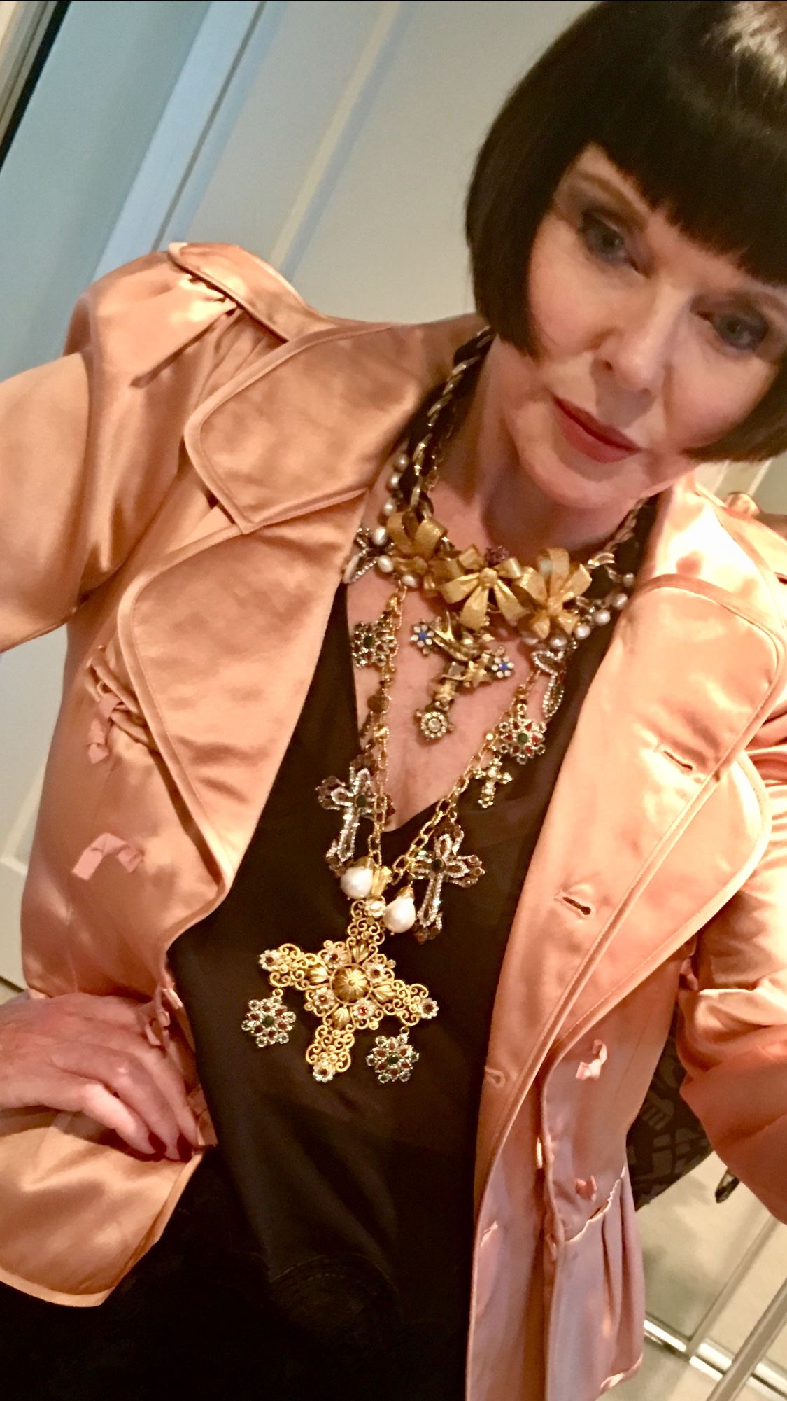 Woman with short dark hair wearing a peach-colored jacket and multiple layered necklaces, posing indoors.