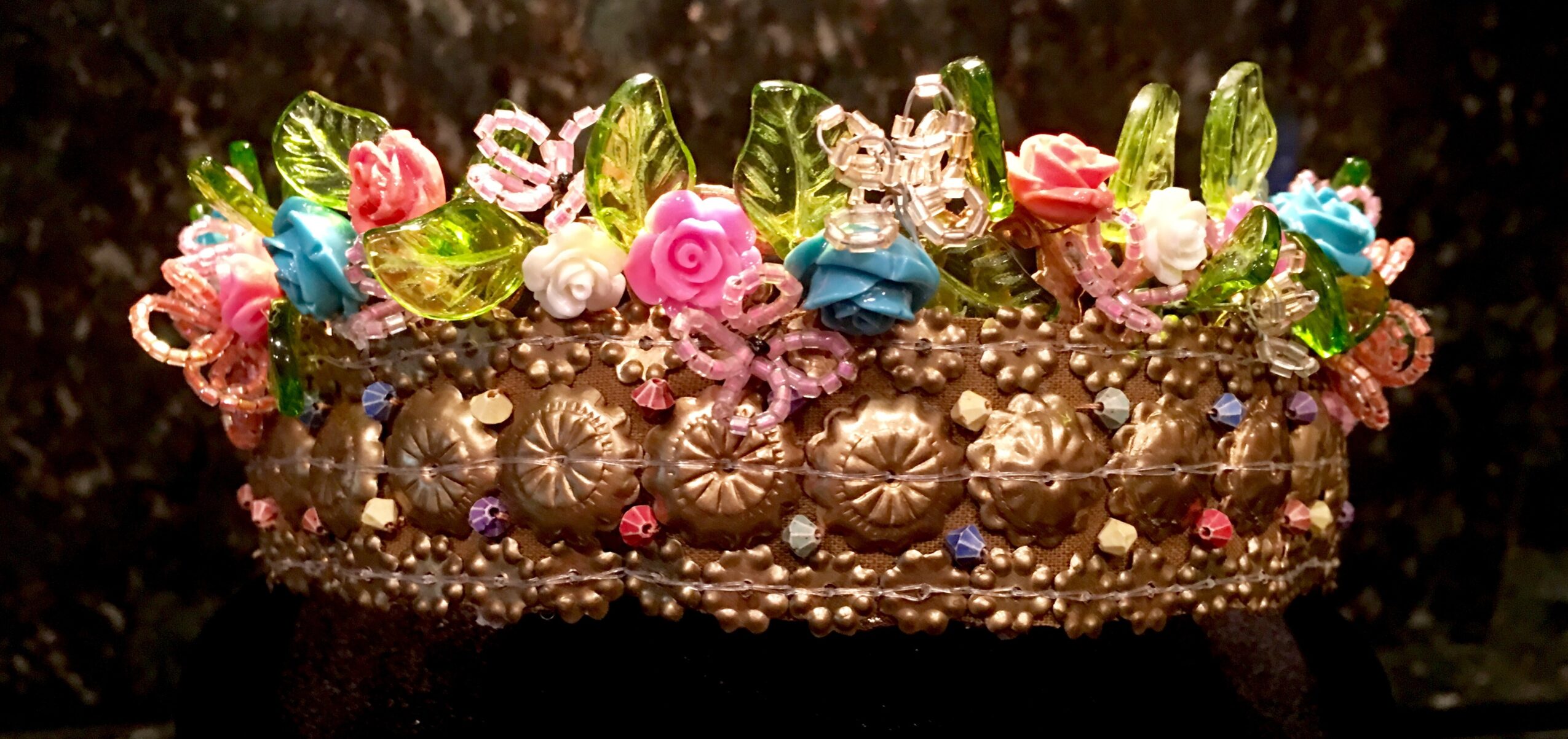 Decorative crown with colorful flowers, pearls, and gemstones, featuring a butterfly ornament, set against a dark background.