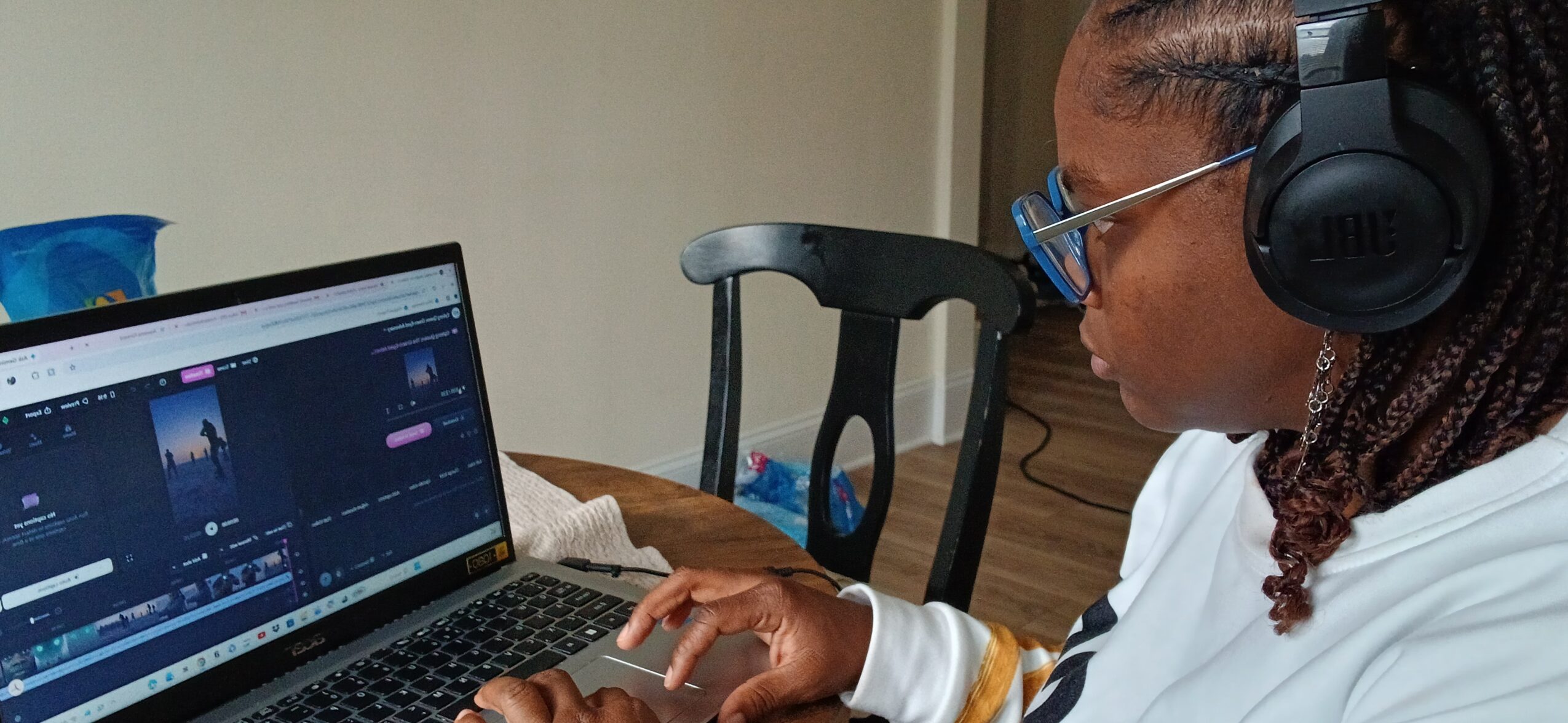 Person wearing headphones working on a laptop with a video editing program open, sitting at a table.