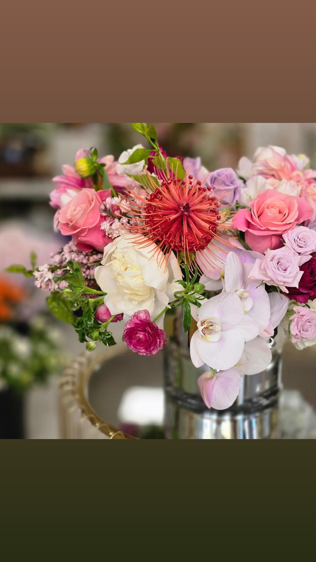 Vase with pink, white, and red flowers including roses and orchids, on a blurred background.