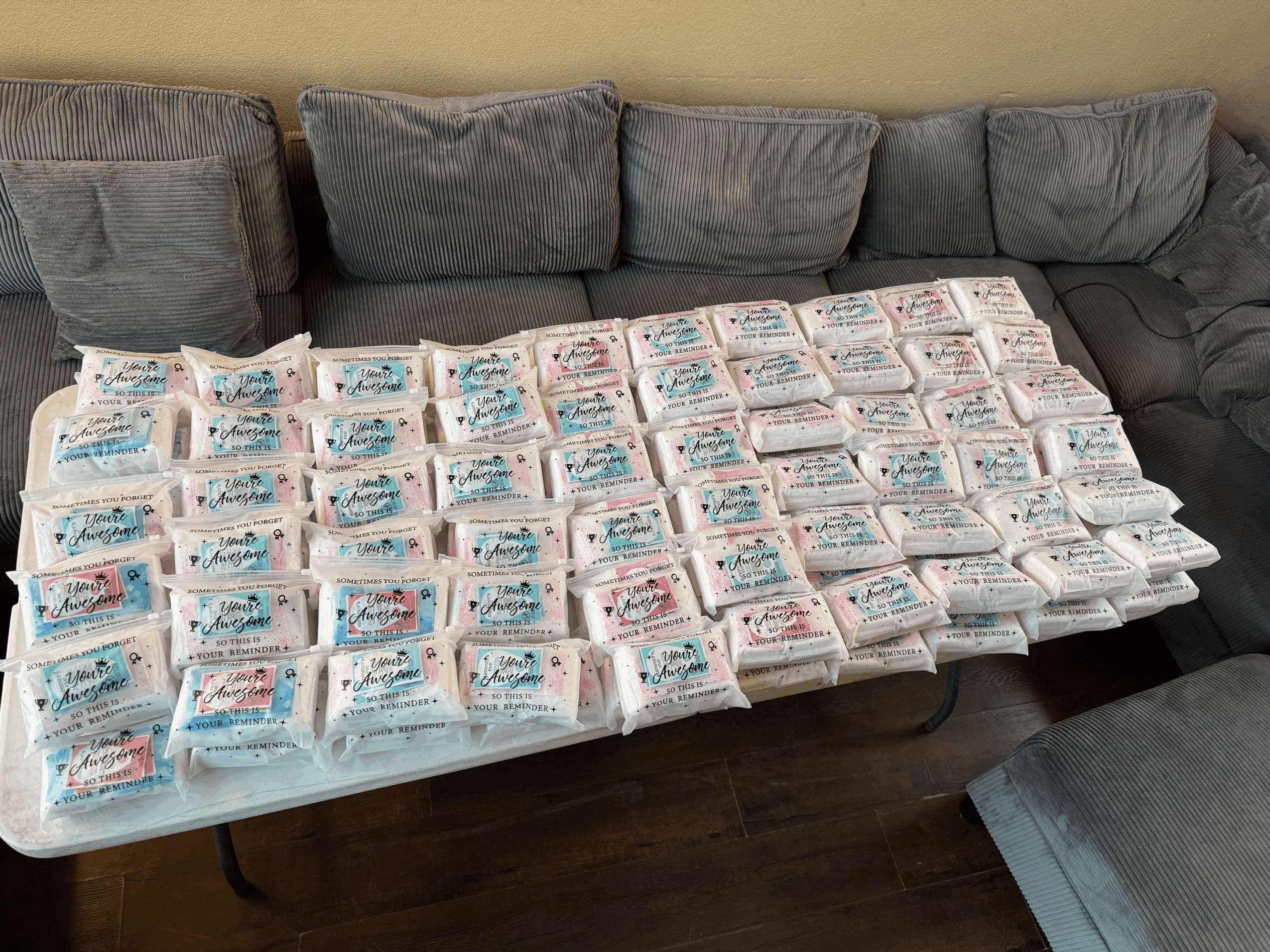 Large table covered with numerous packages, in front of a gray sofa with cushions, in a living room setting.