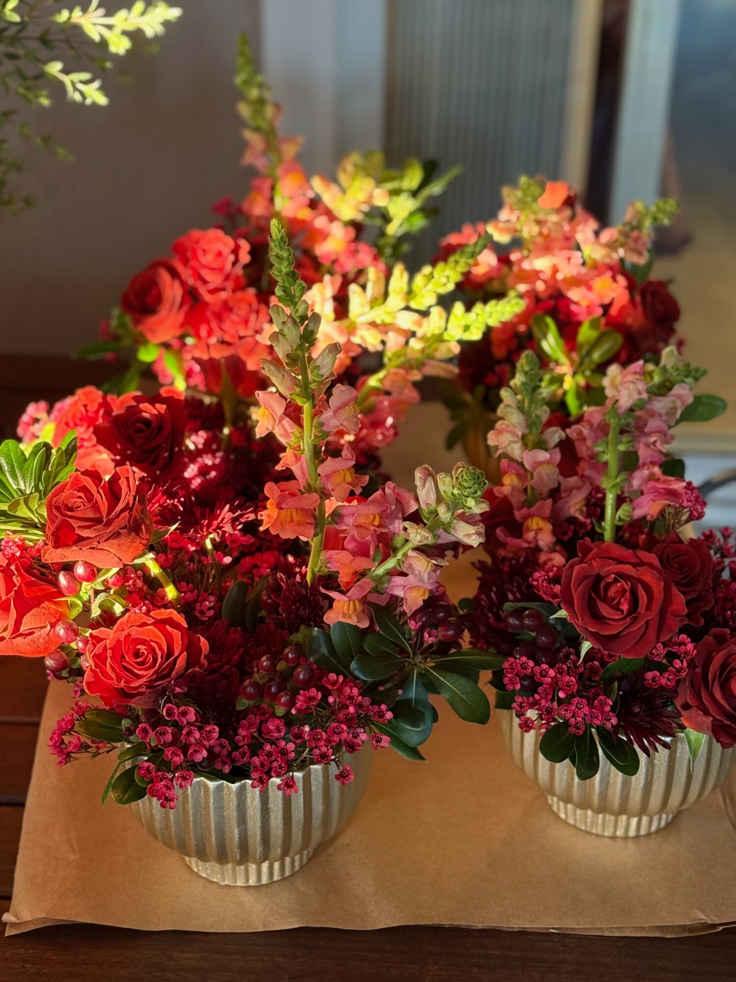 Two striped pots with pink and red flowers on a table, sunlight shining on the arrangement.