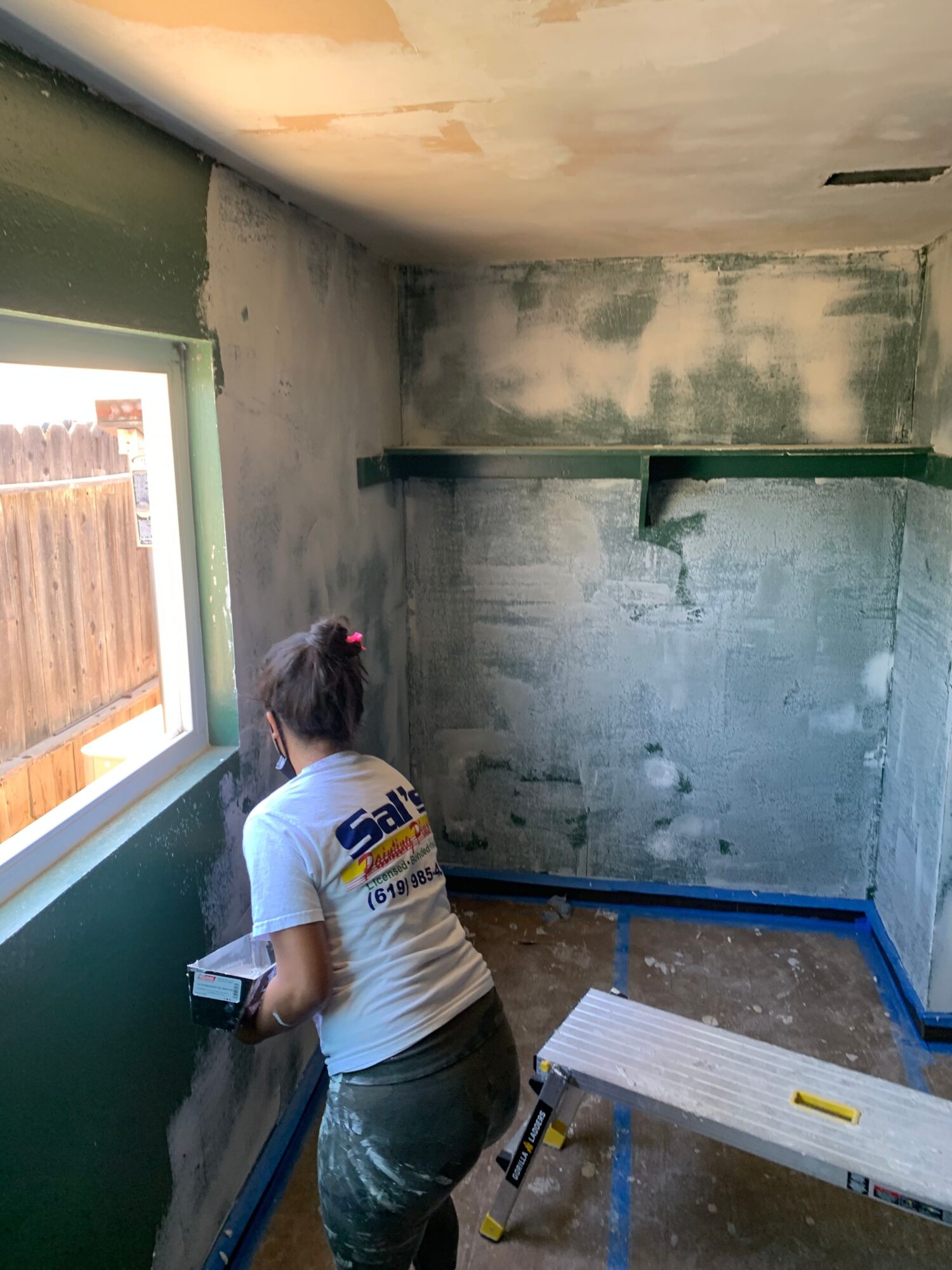 Person working on construction or renovation, with tools and materials around, in a partially finished room.