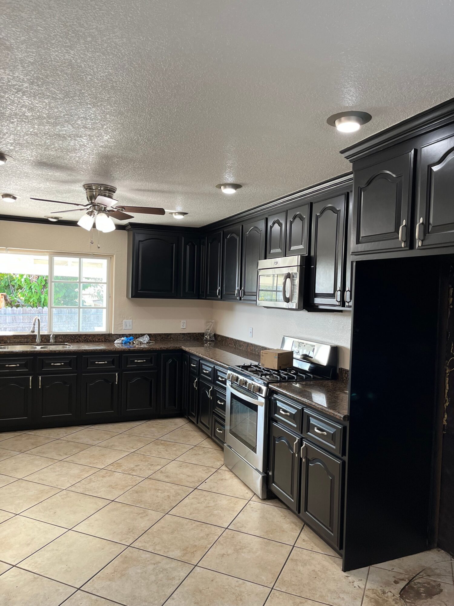 Kitchen with black cabinets, a window, and tiled floor, viewed from an angle.