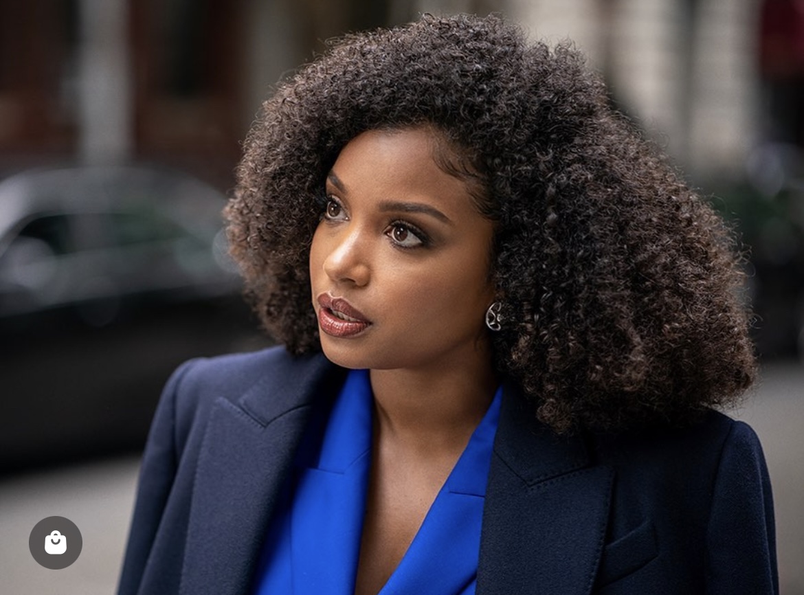Woman with curly hair wearing a blue blazer outdoors, looking to the side.