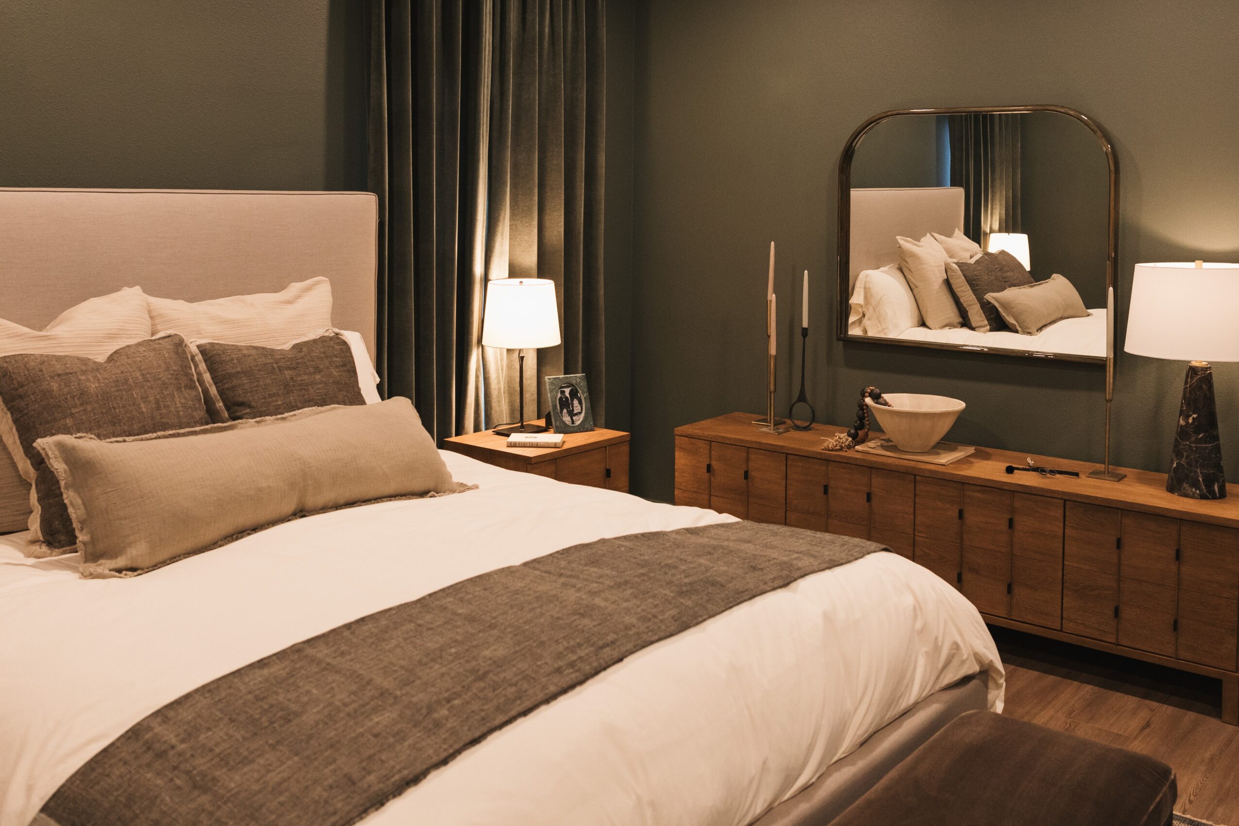 Bedroom with bed, pillows, bedside table, mirror, and dresser, decorated in neutral tones.