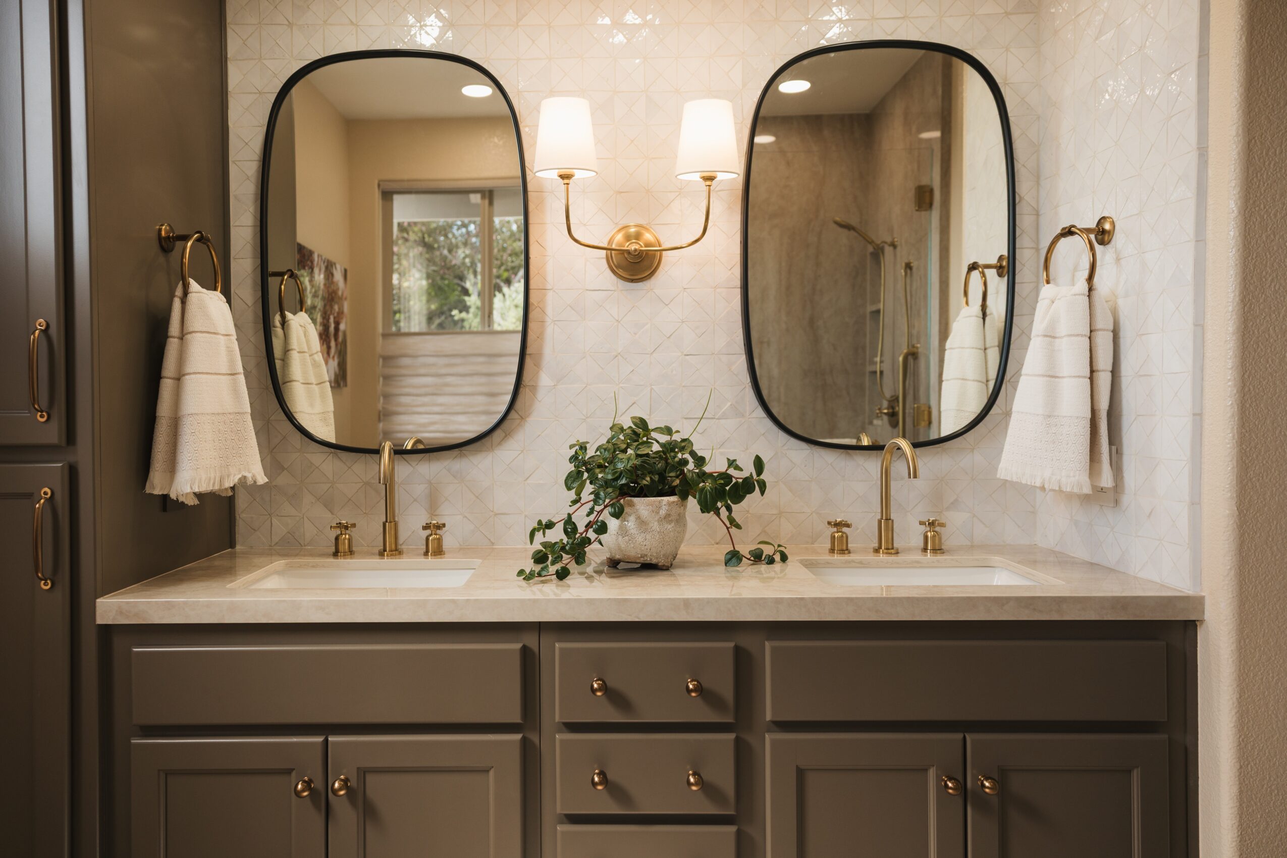 Double sink bathroom vanity with two mirrors, a wall-mounted light fixture, and a potted plant between sinks.