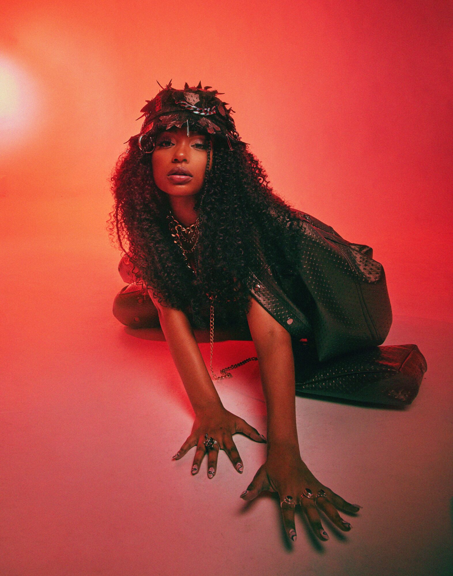 Woman with curly hair, wearing a crown of leaves, lying on the floor with a red background.