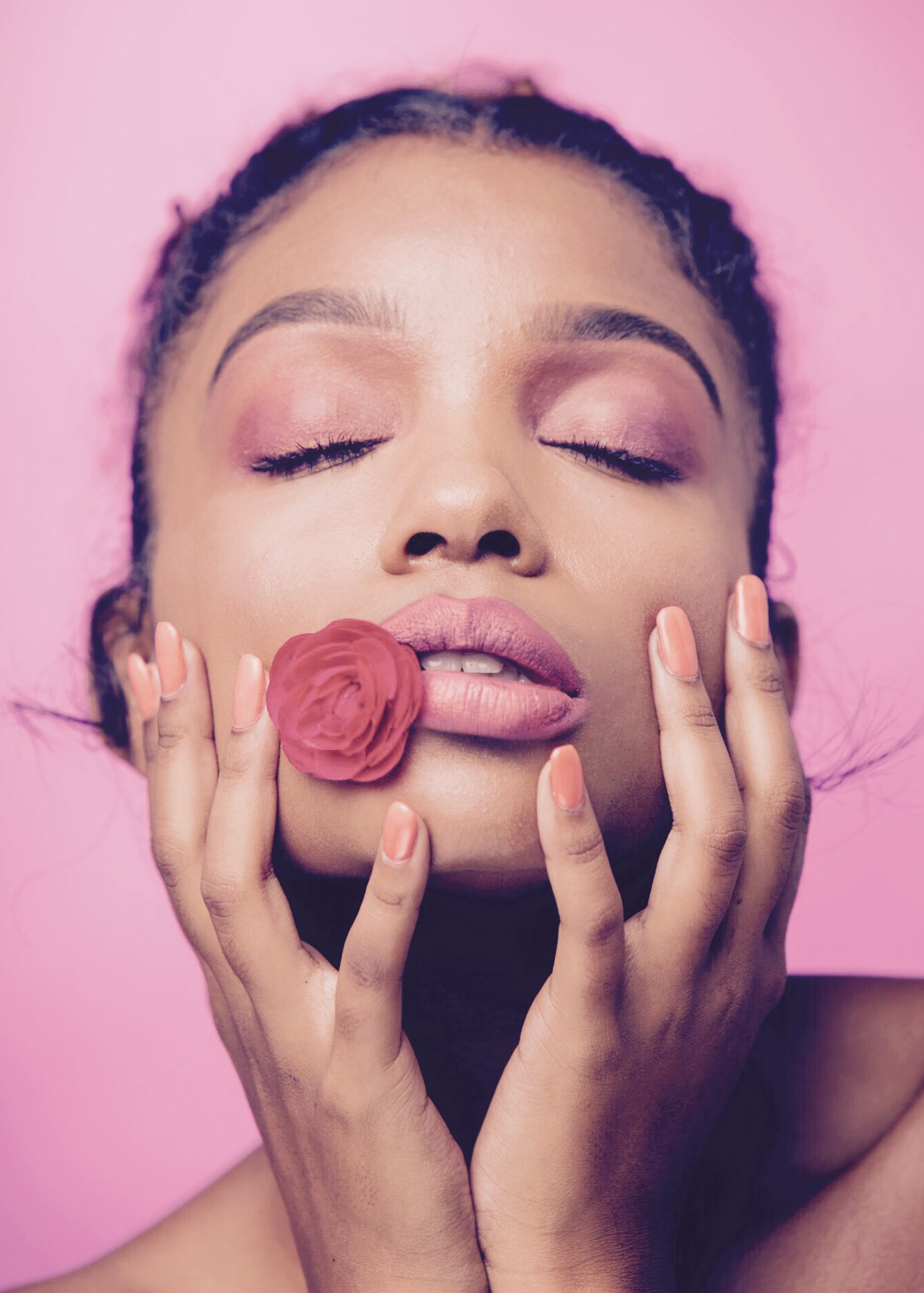 Close-up of a woman with eyes closed, holding a pink flower near her lips, against a pink background.
