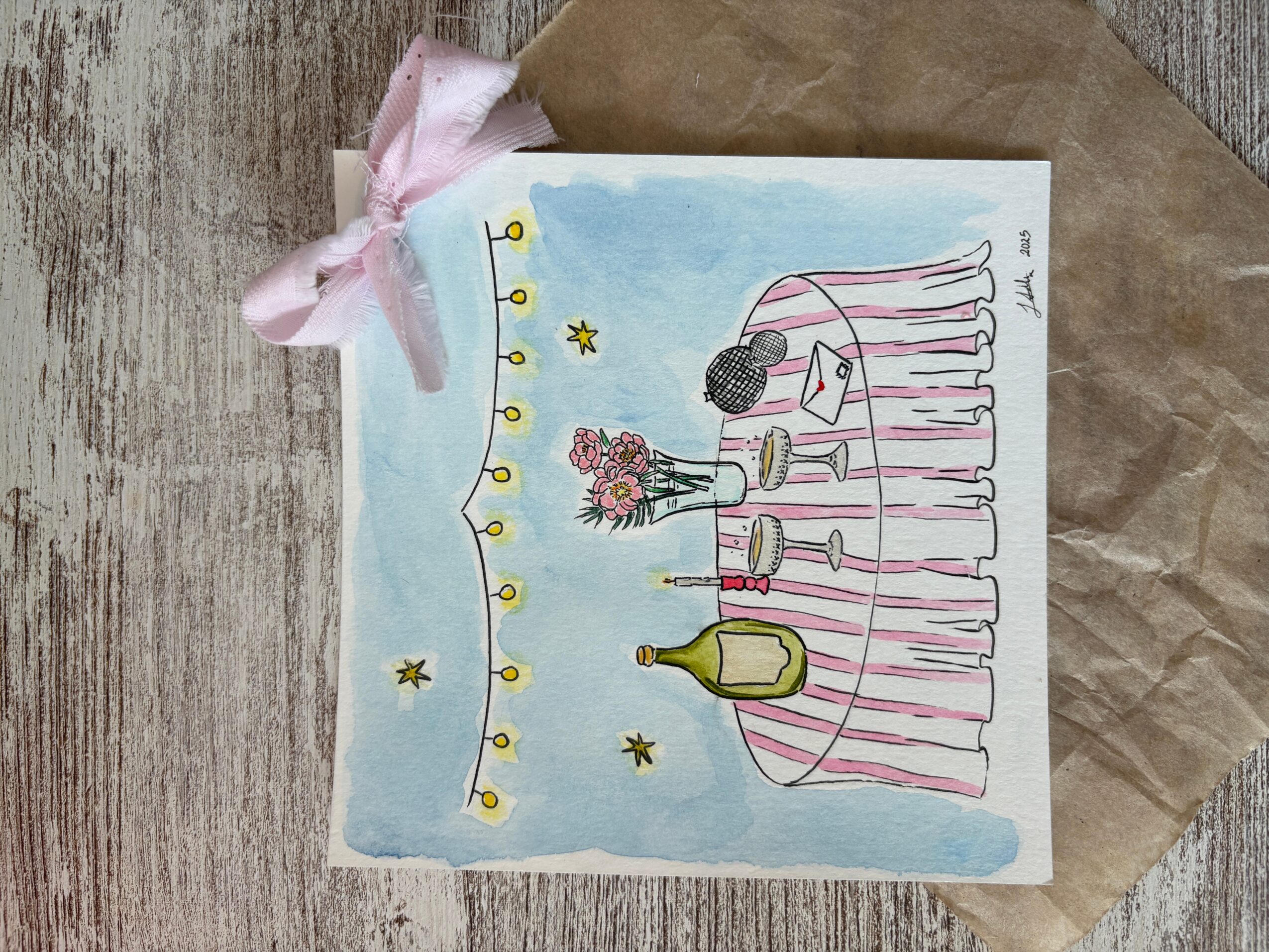 A colorful illustration of a table with a pink and white striped tablecloth, decorated with flowers, bottles, and glasses, under a blue sky with stars and a string of lights.