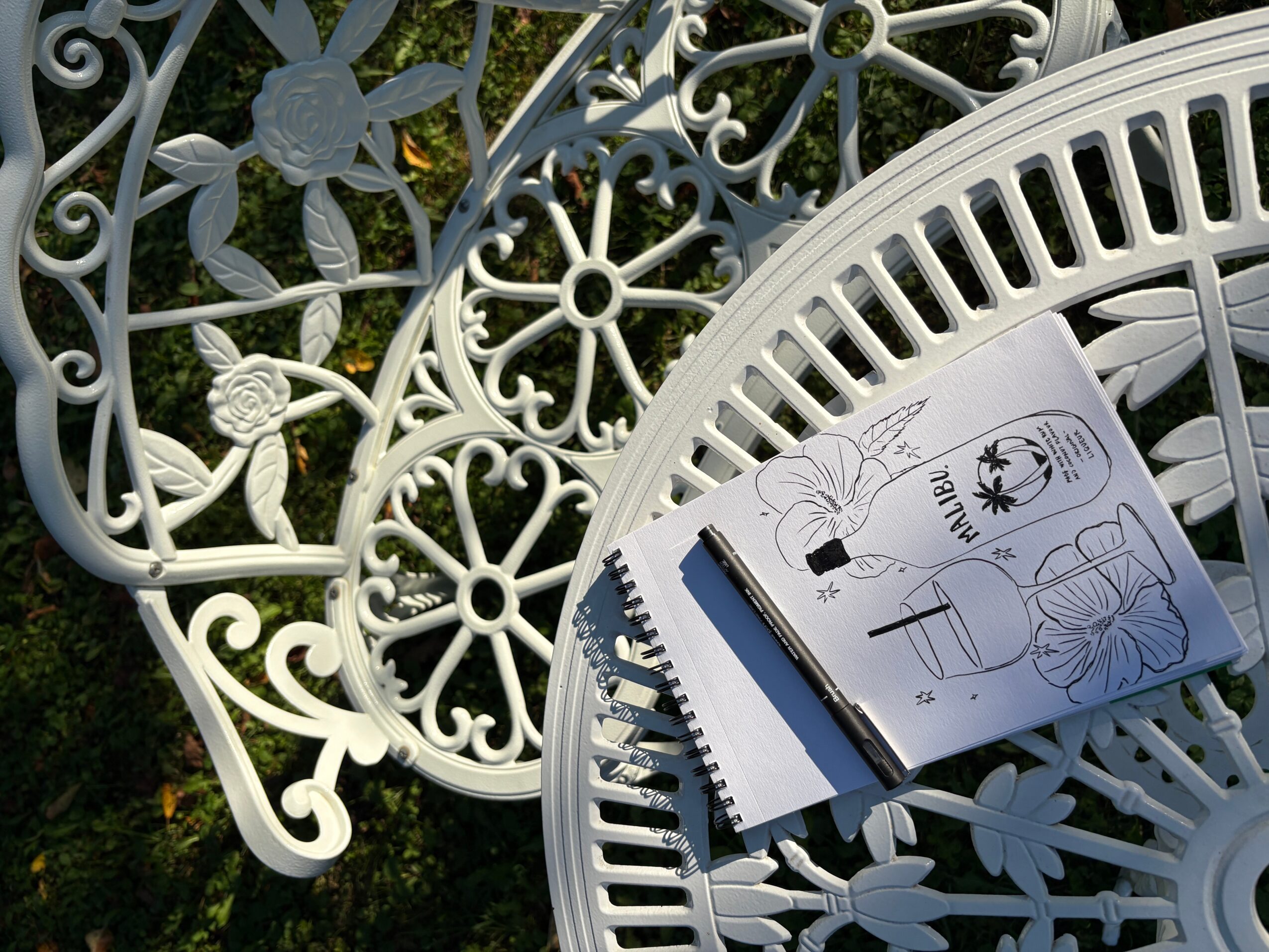 White ornate metal table and chair with an instruction booklet on the table, outdoors with greenery in the background.
