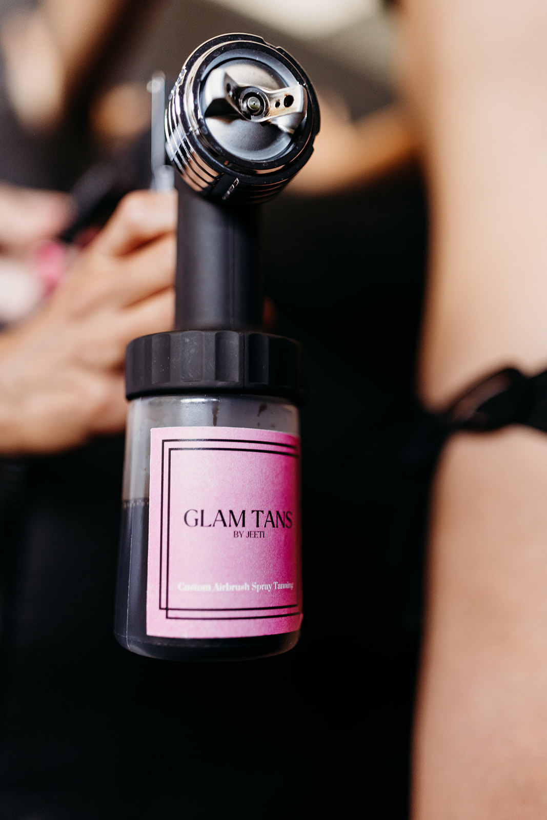 Close-up of a handheld device with a pink label reading 'GLAM TANS' and a black top, held by a person.