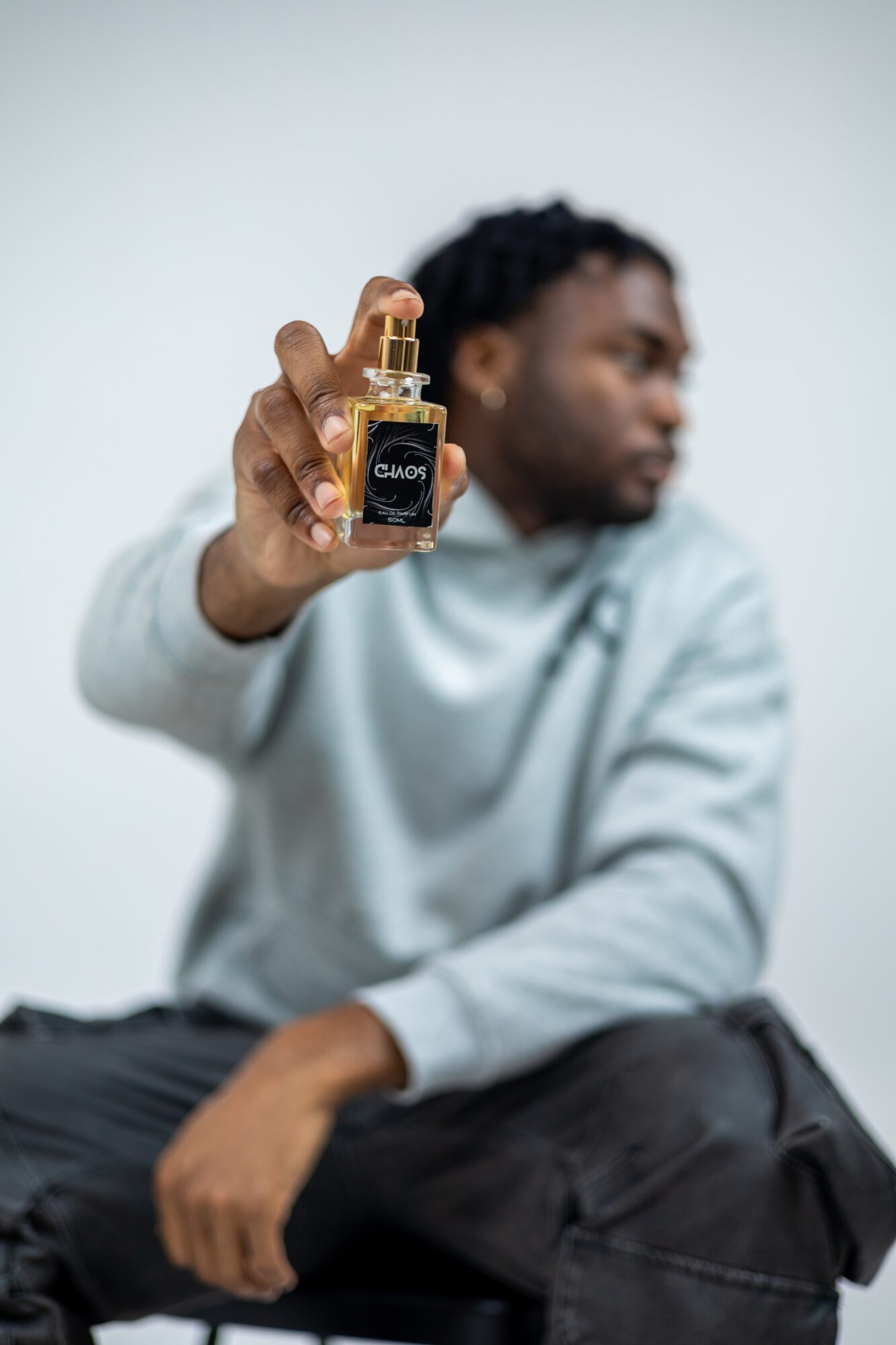 Person holding a small bottle with a spray nozzle, focus on the bottle, blurred background, person looking away.