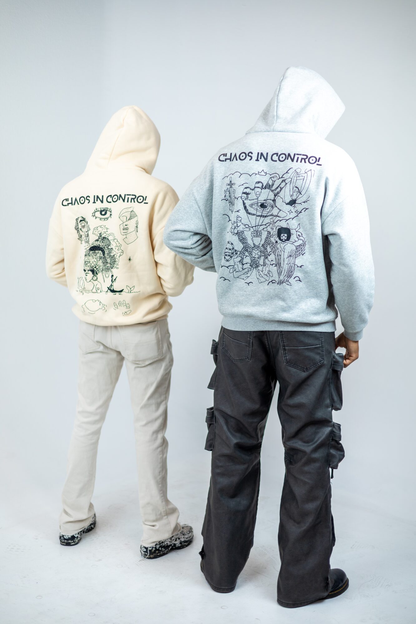Two people wear hoodies with graphic designs and text, facing away from the camera, against a plain background.