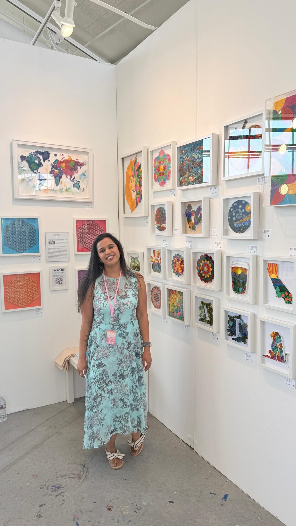 Woman in a long floral dress standing in an art gallery with colorful framed artworks on white walls.
